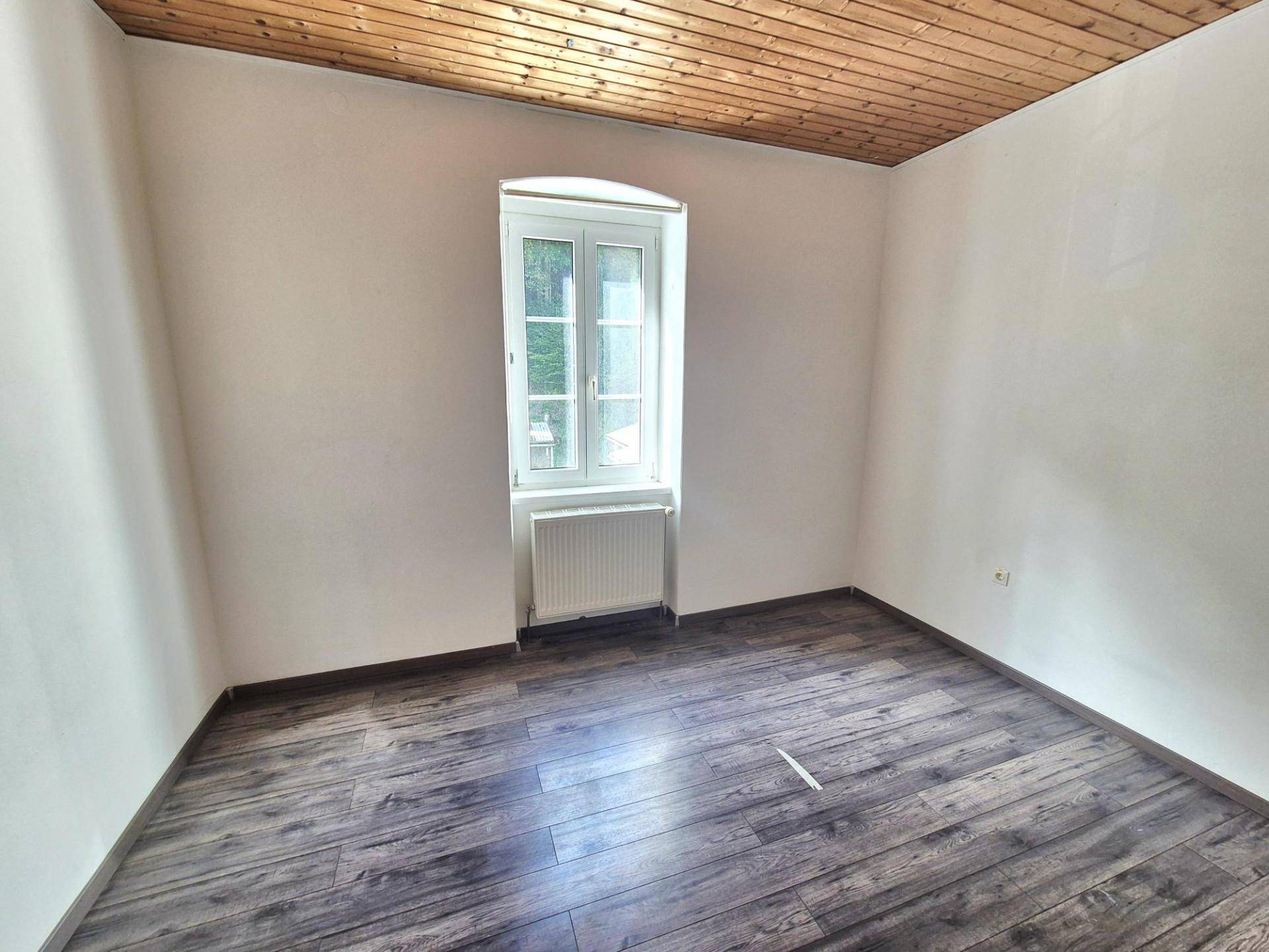 Schlafzimmer mit Holzbalkendecke, dunklem Laminatboden und einem Fenster.