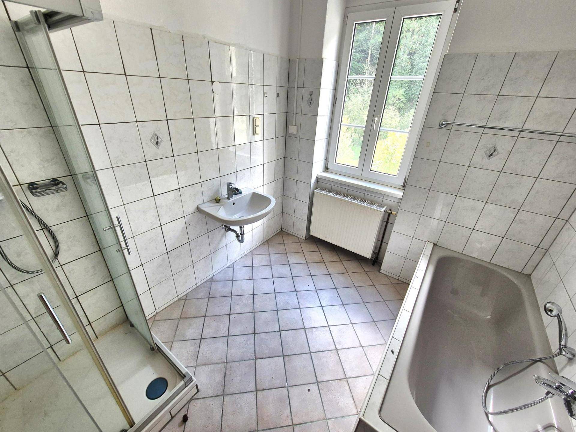 Badezimmer mit Badewanne, Duschkabine, Waschbecken und Fenster, komplett gefliest.