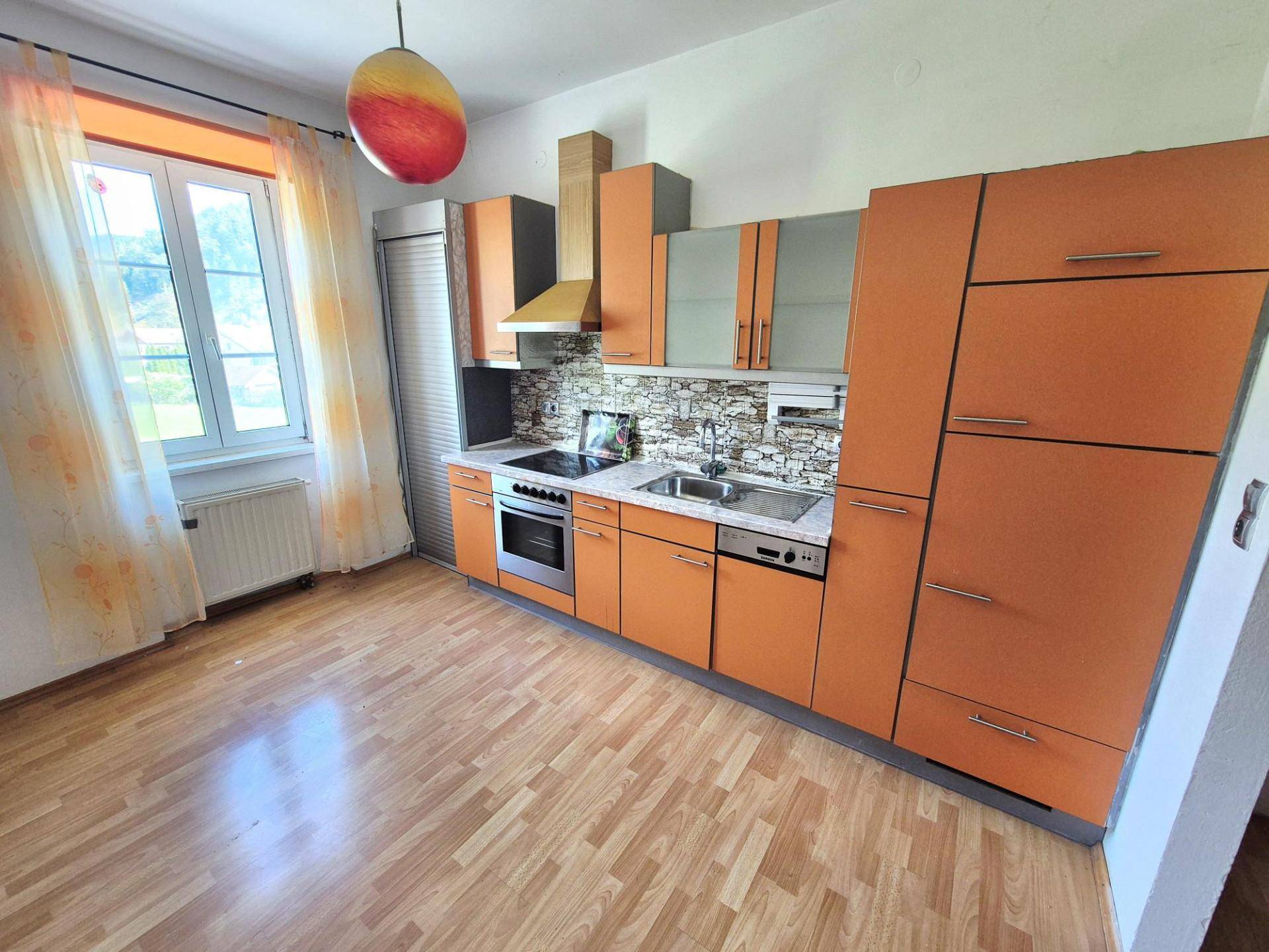 Geräumige Küche mit orangefarbenen Fronten, Laminatboden und großem Fenster.