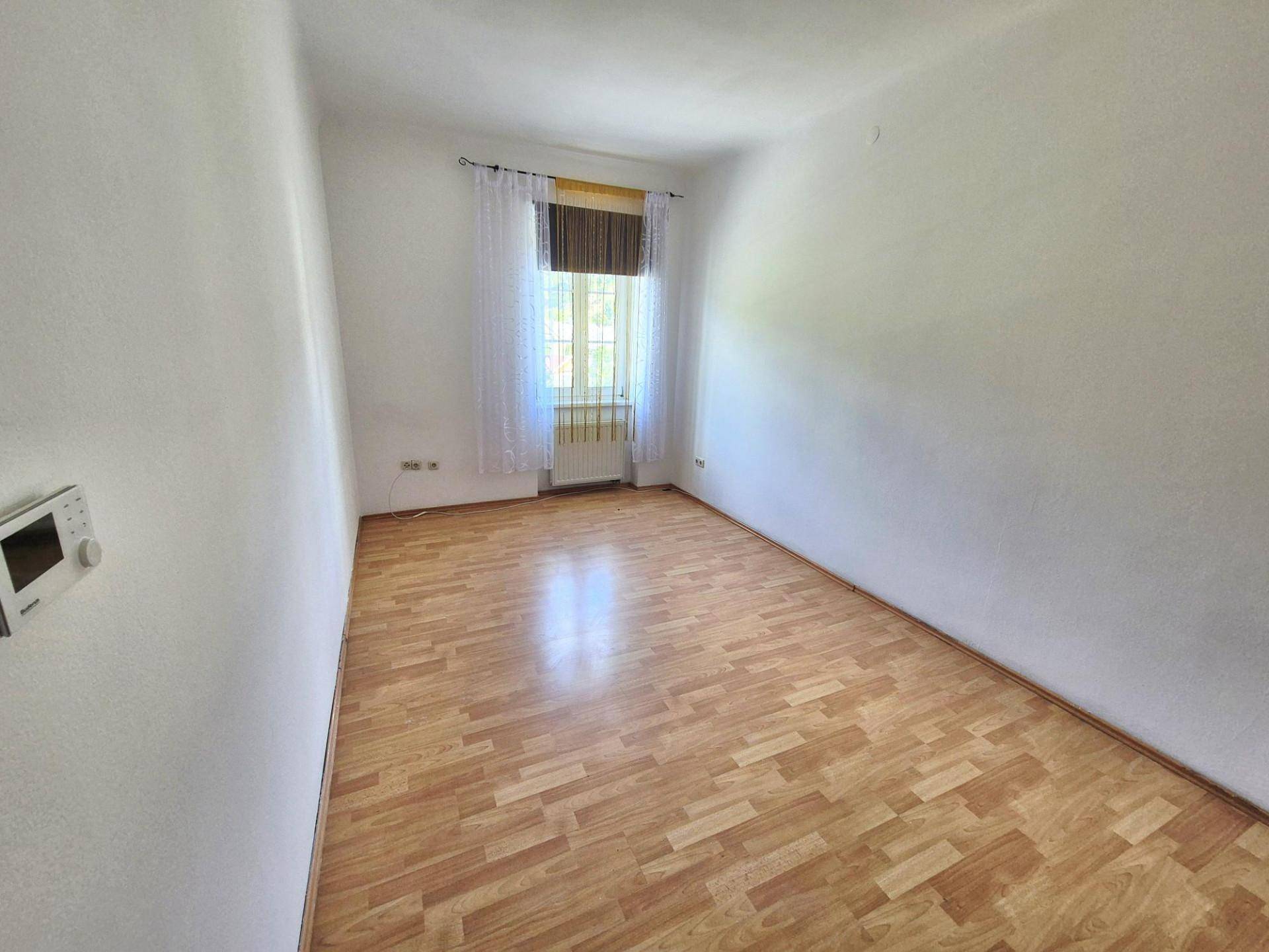 Schlafzimmer mit Laminatboden, weiß gestrichenen Wänden und einem Fenster mit Vorhängen.