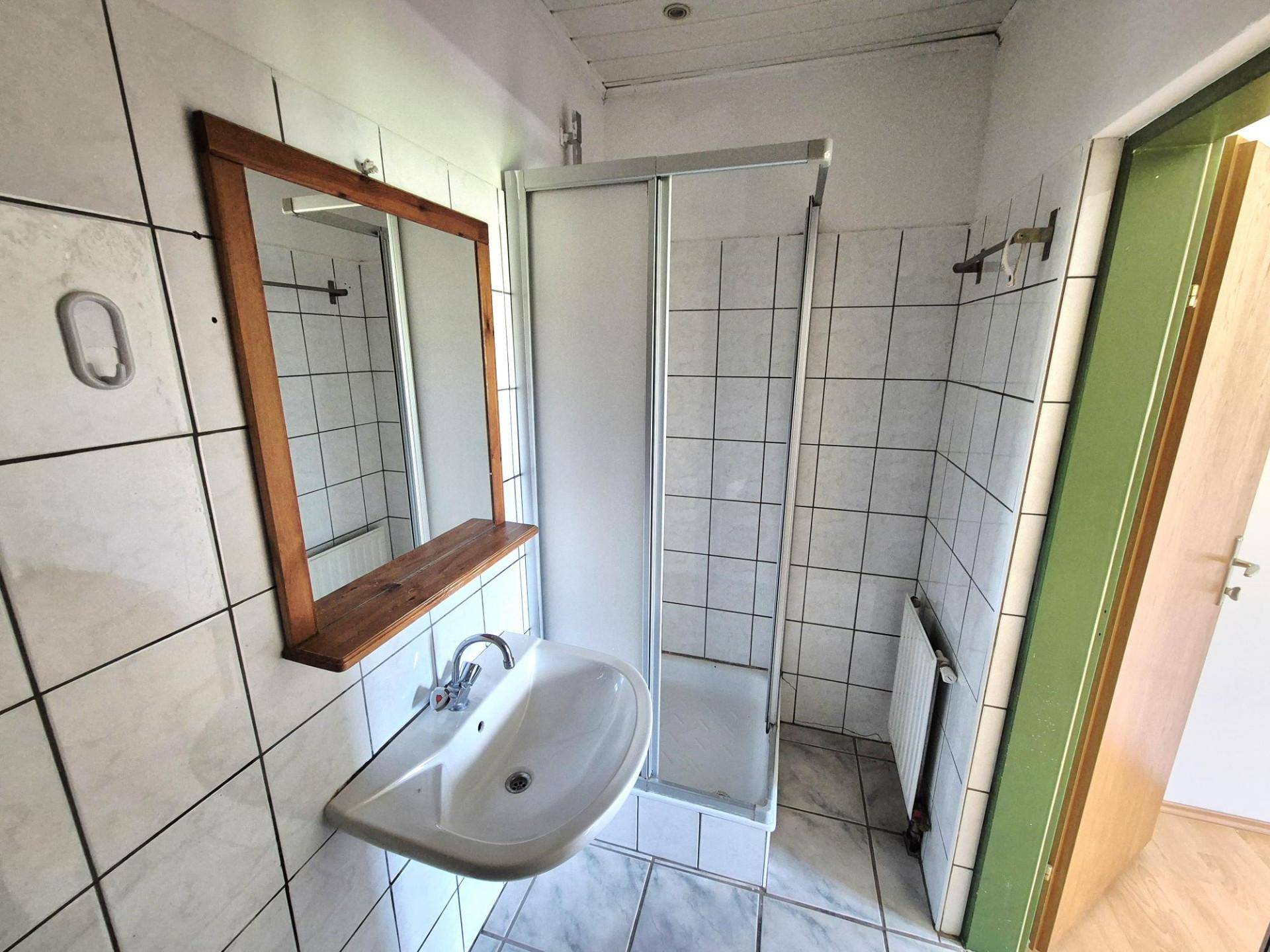 Badezimmer mit Duschkabine, Waschbecken und Spiegel, komplett gefliest.