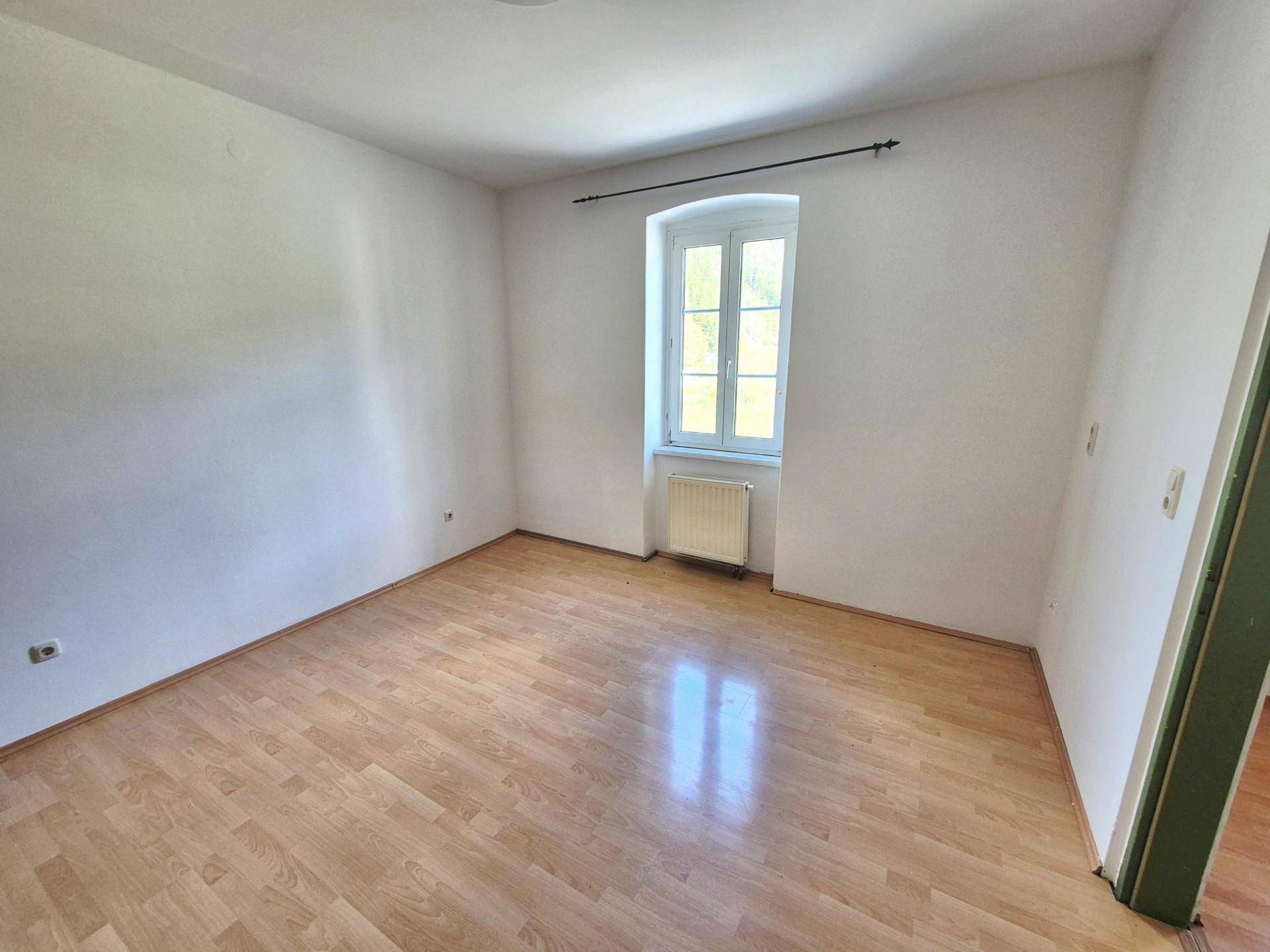 Schlafzimmer mit Laminatboden, weiß gestrichenen Wänden und einem Fenster.