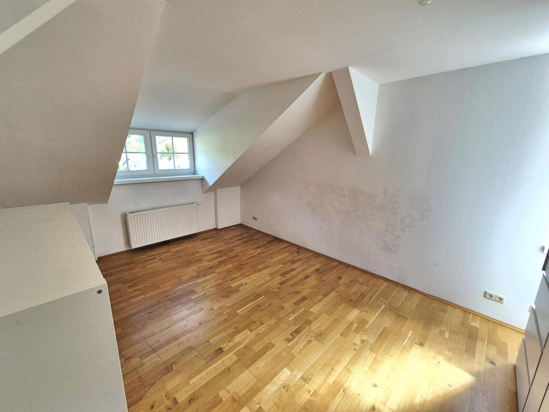 Dachgeschoss-Schlafzimmer mit Holzboden, schrägen Wänden und Fenster.
