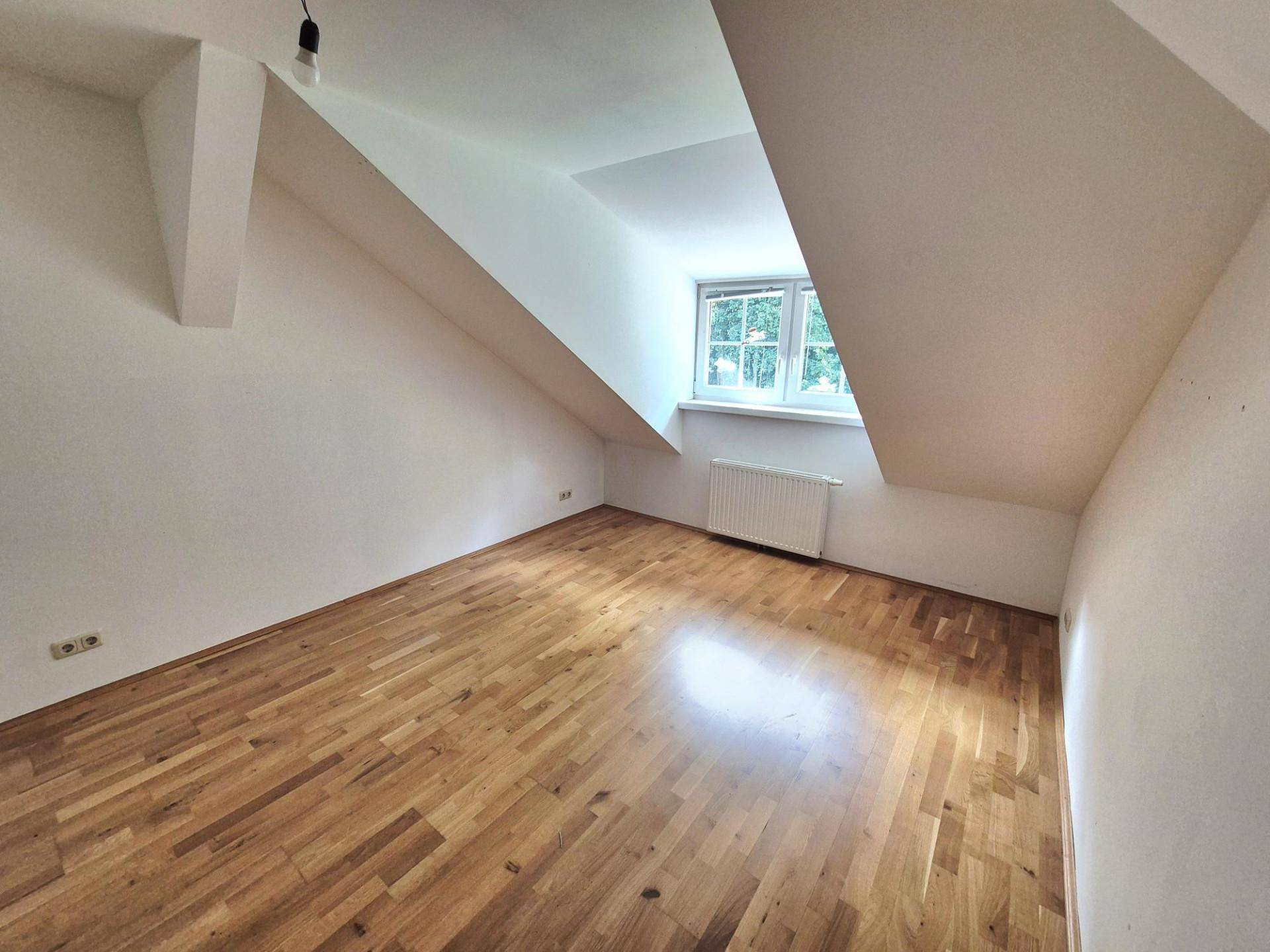 Dachgeschoss-Schlafzimmer mit Holzboden, schrägen Wänden und Fenster.