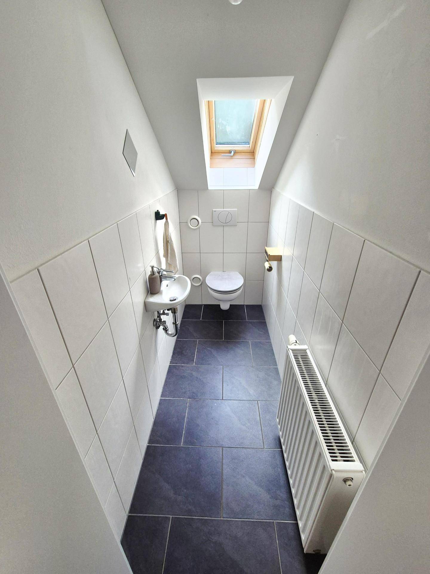 Kleines Gäste-WC mit Toilette, Waschbecken und einem Dachfenster für natürliches Licht.