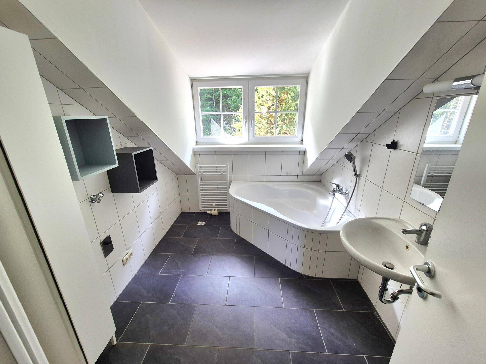 Modernes Badezimmer mit Badewanne, Waschbecken und Fenster unter einer Dachschräge.