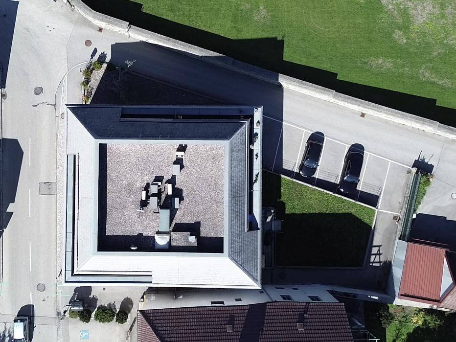 Senkrechte Luftaufnahme eines modernen Gebäudes mit Flachdach und Parkplätzen in der Umgebung.