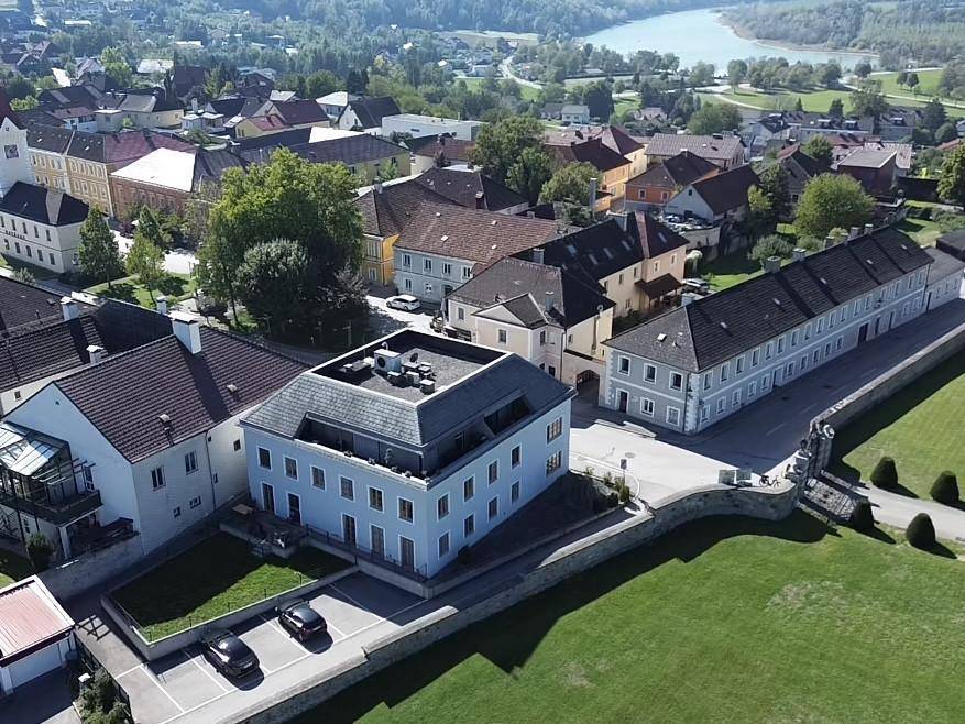 Panoramablick aus der Luft auf ein Dorf mit Fluss im Hintergrund und umliegender grüner Landschaft.