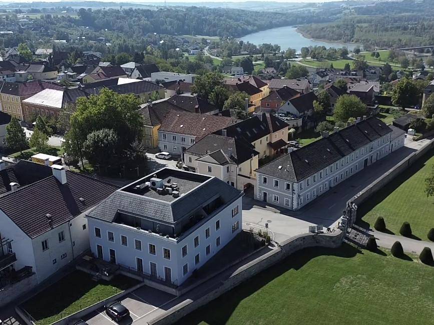 Weitläufige Luftaufnahme eines Dorfes mit einem Fluss in der Ferne und grüner Hügellandschaft.