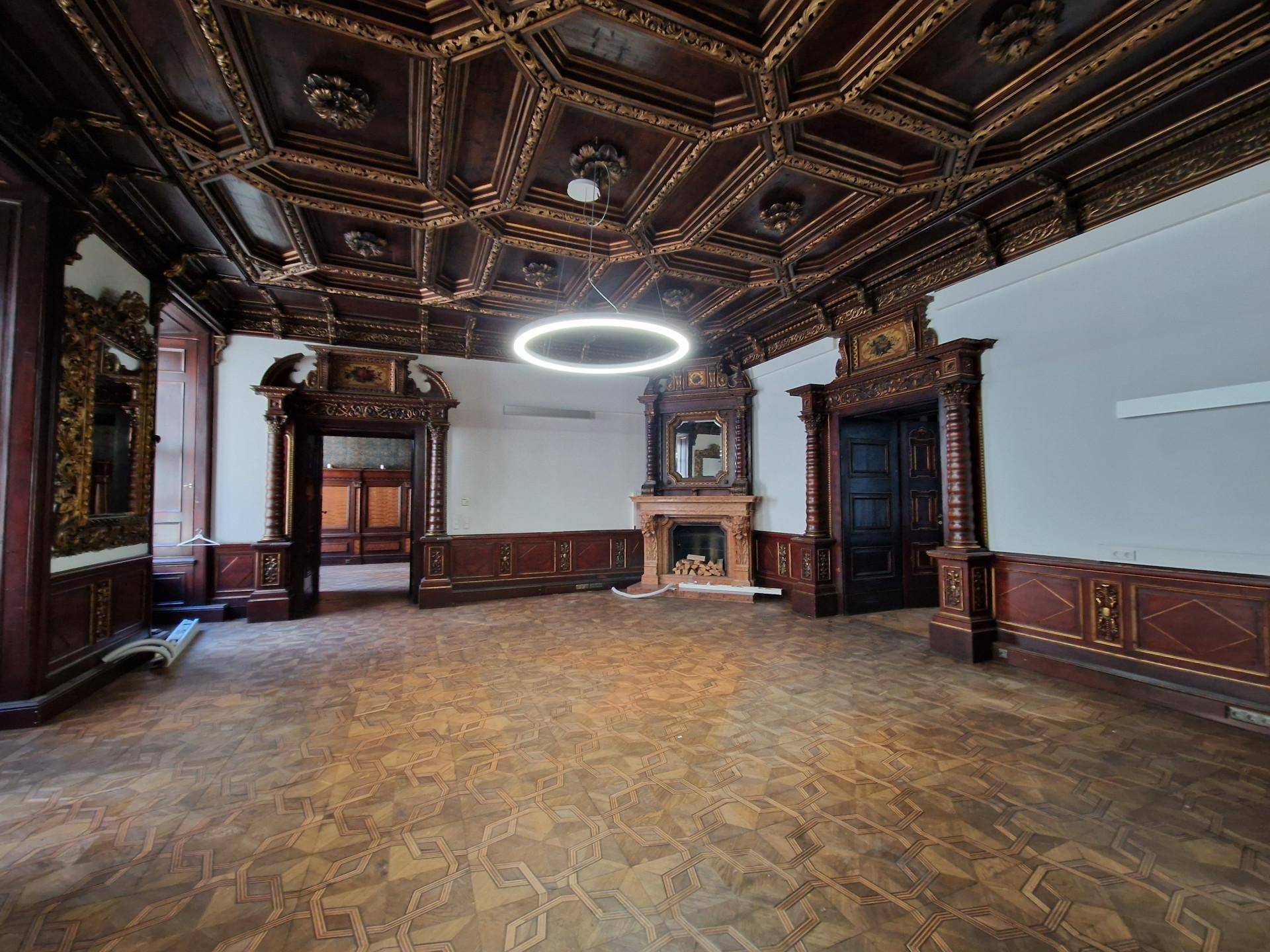 Geräumiger Raum mit aufwendiger Holztäfelung, Kassettendecke und einem dekorativen Kamin.