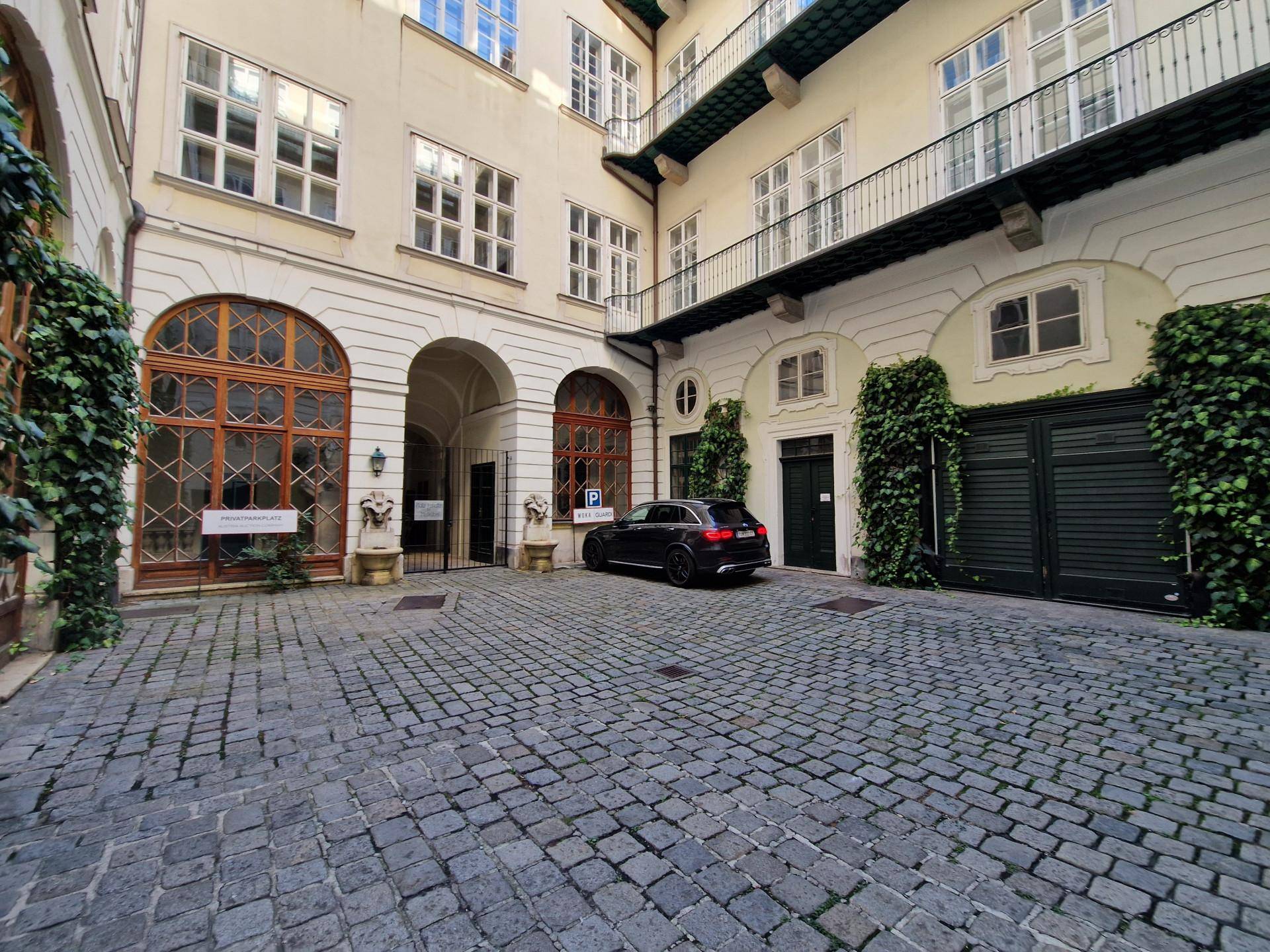 Historischer Innenhof mit Kopfsteinpflaster, Balkonen und einem geparkten Auto.