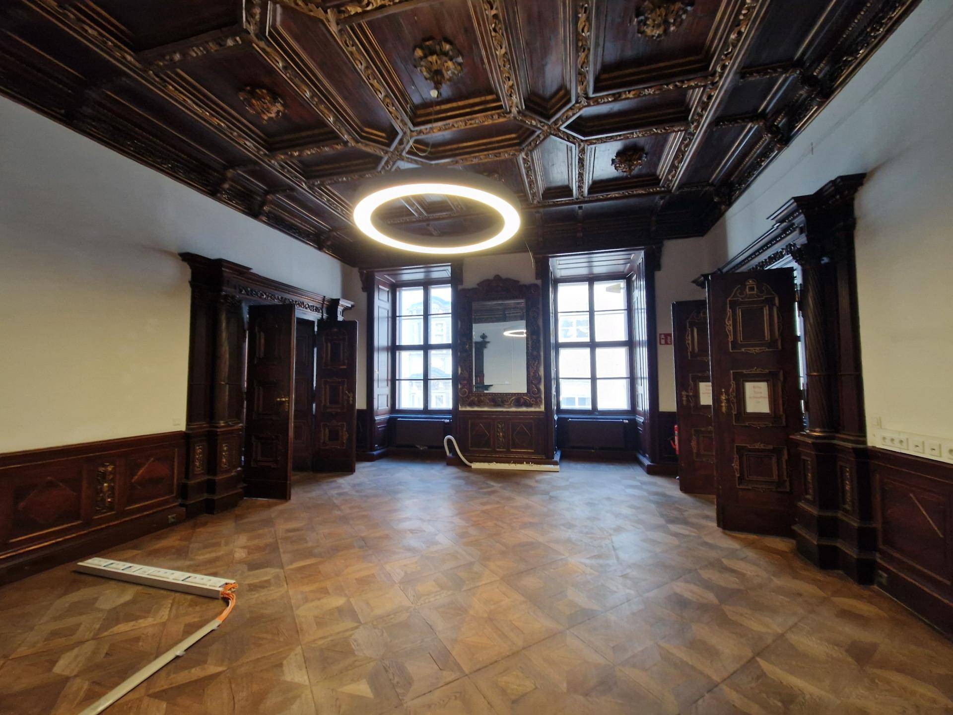 Geräumiger Raum mit dunkler Holztäfelung, Kassettendecke und einem modernen Deckenlicht.