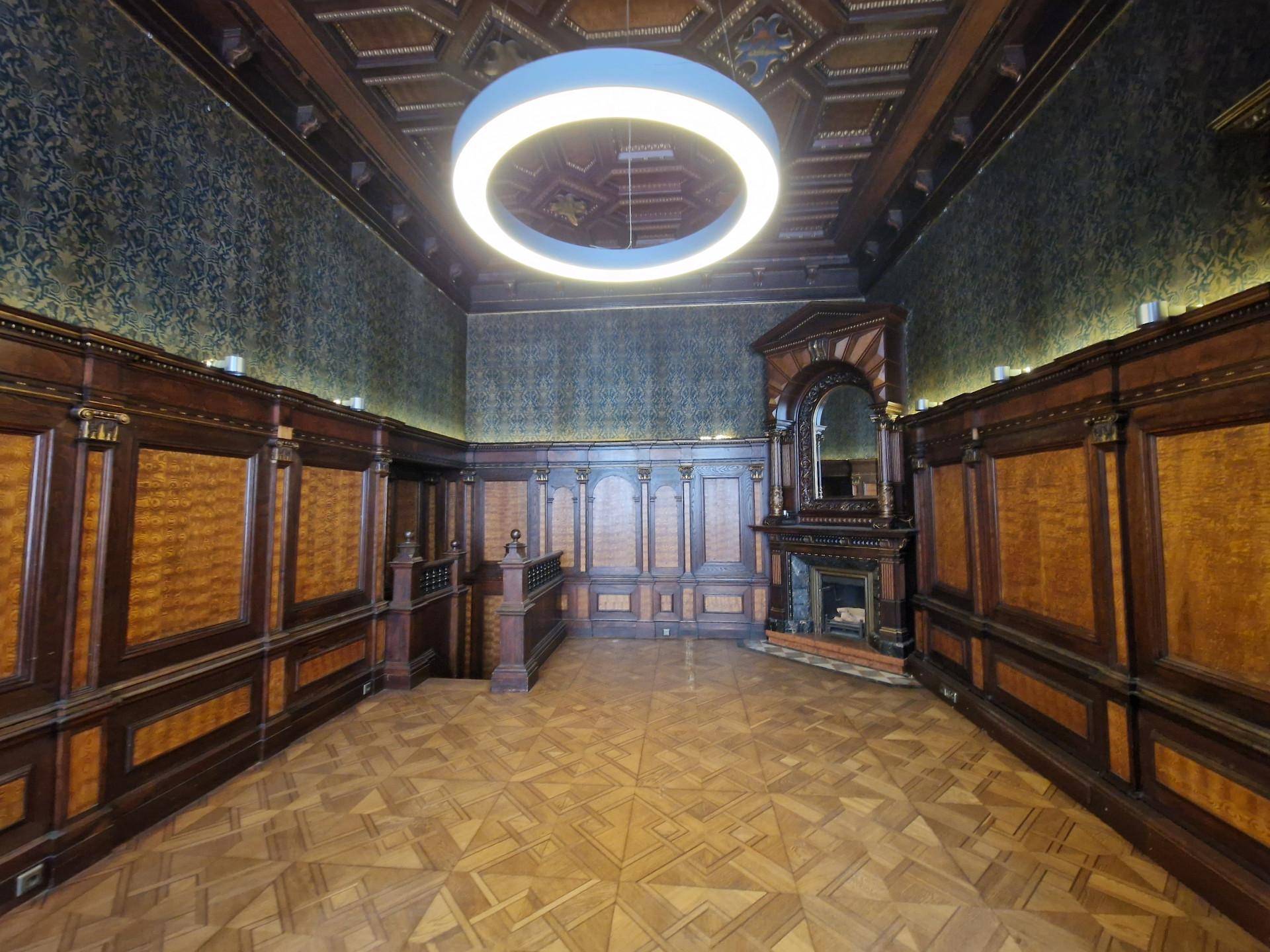 Geräumiger Raum mit dunkler Holztäfelung, gemusterter Tapete und einer Kassettendecke mit modernem Licht.
