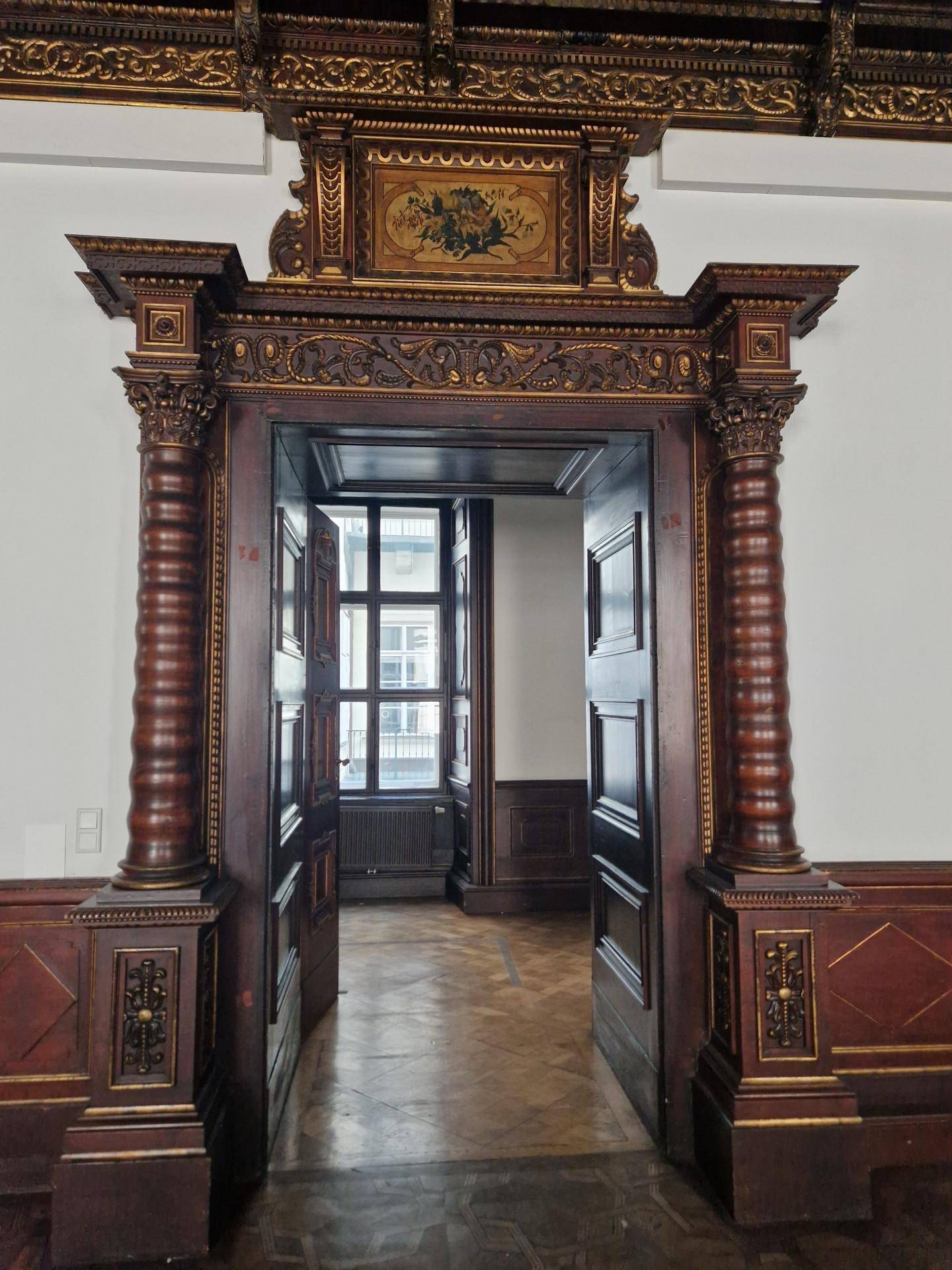 Opulenter Türrahmen aus dunklem Holz mit Säulen und Verzierungen, der zu einem weiteren Raum führt.
