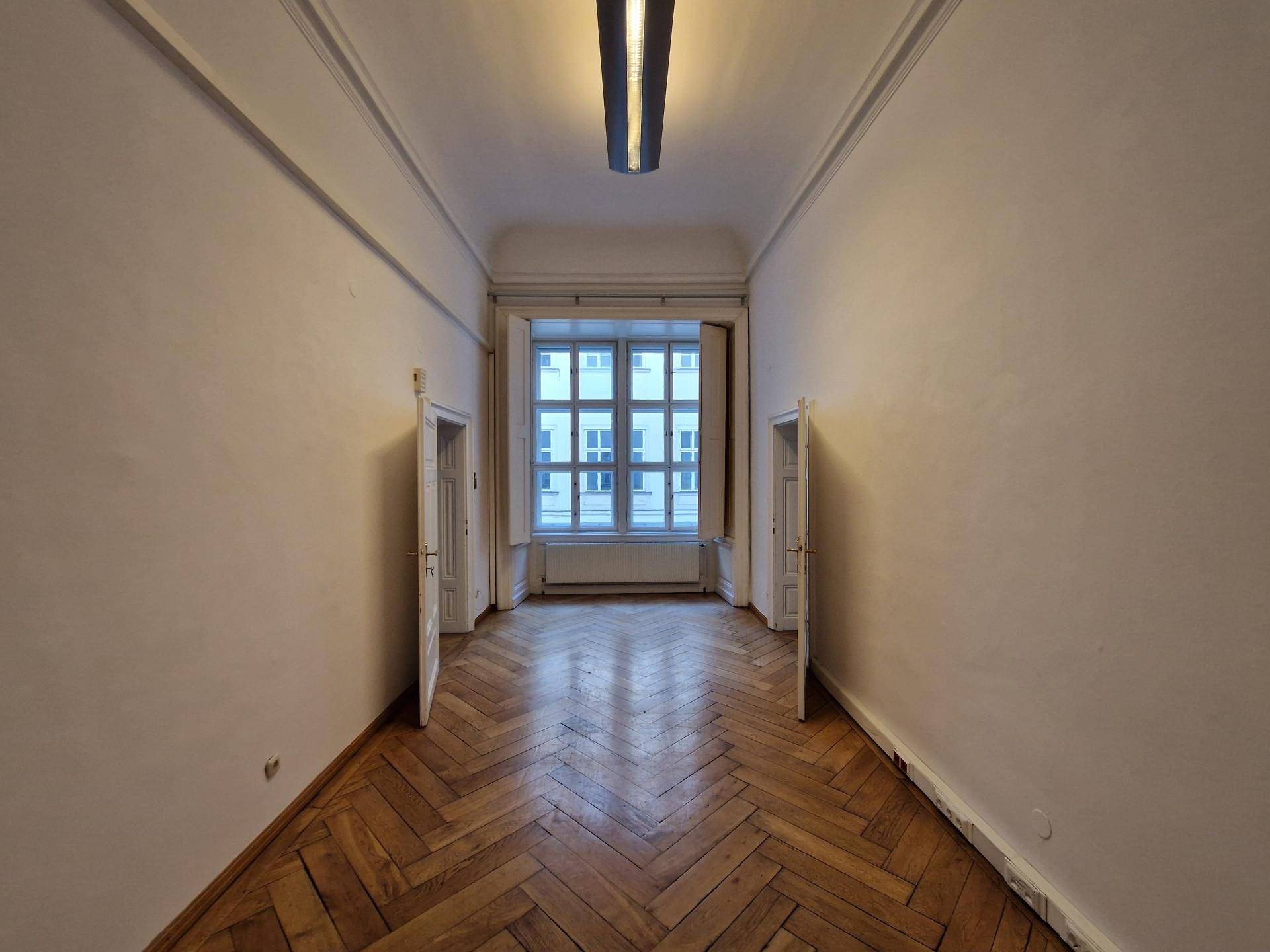 Langer Flur mit Fischgrätparkett, hohen Decken und einem großen Fenster am Ende.