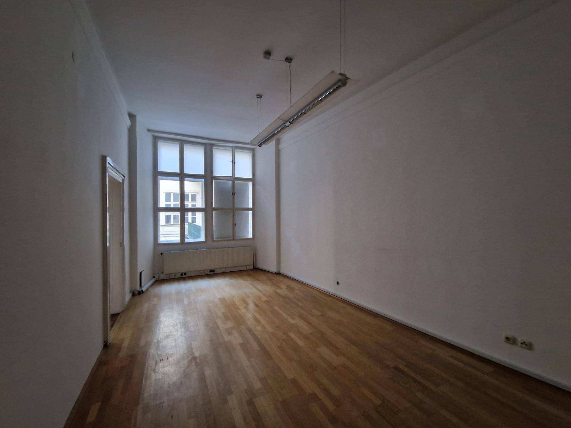 Heller Raum mit Holzboden, hohen Decken und einem großen Fenster.