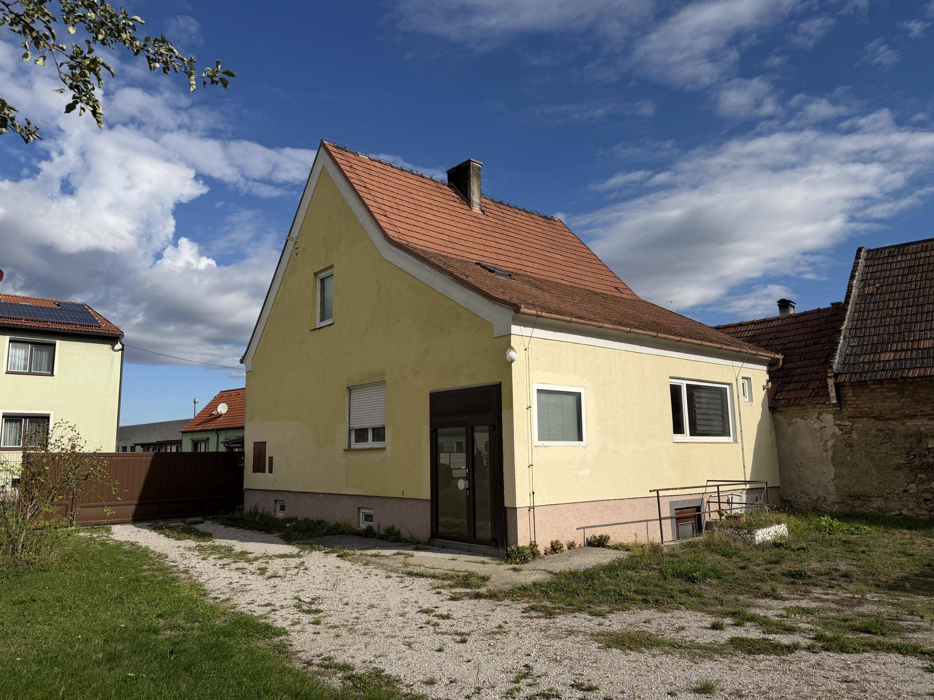 Seitenansicht des gelben Hauses mit Rollläden und einem kleinen Zugang zum Grundstück.