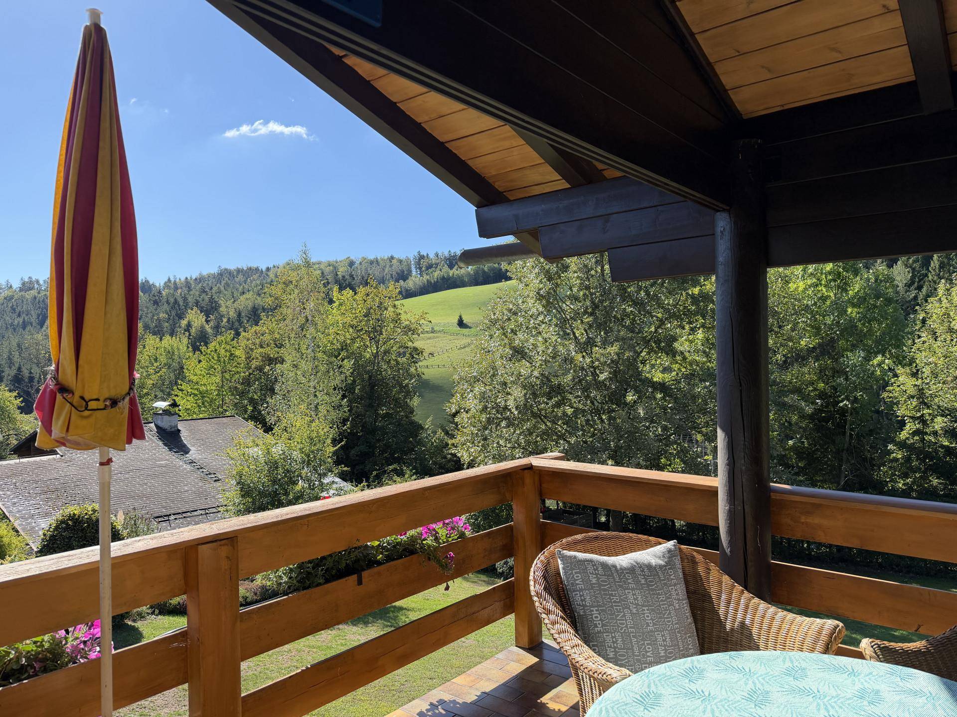 Sonniger Balkon mit Holzbalken und weitem Blick über die grüne Hügellandschaft.