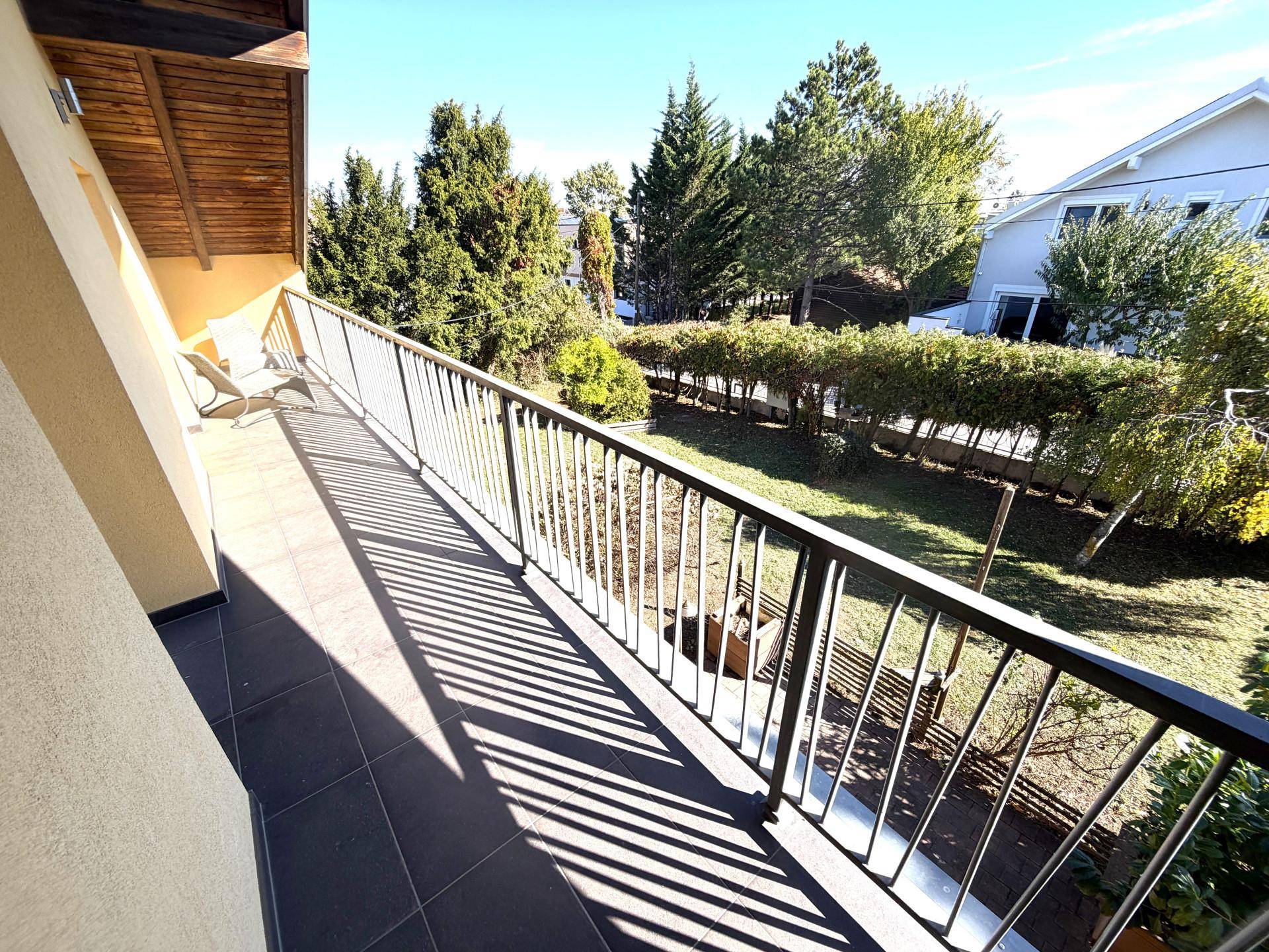 Balkon mit Blick auf den grünen Garten und die umliegende Natur unter strahlendem Sonnenschein.