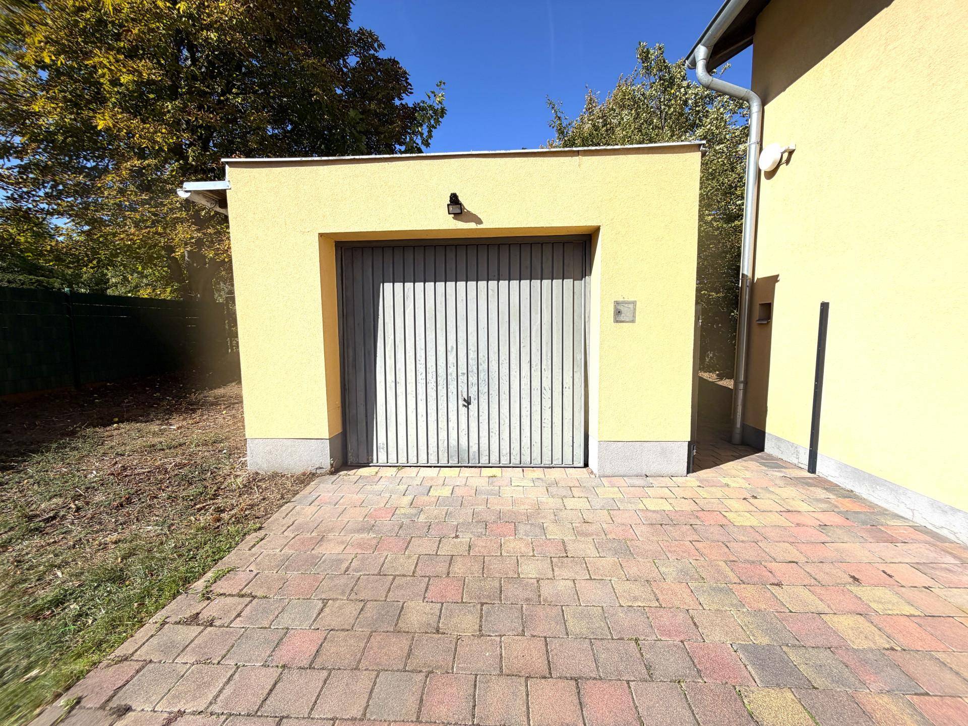 Separate Garage mit geschlossenem Tor und gepflasterter Zufahrt neben dem Wohnhaus.