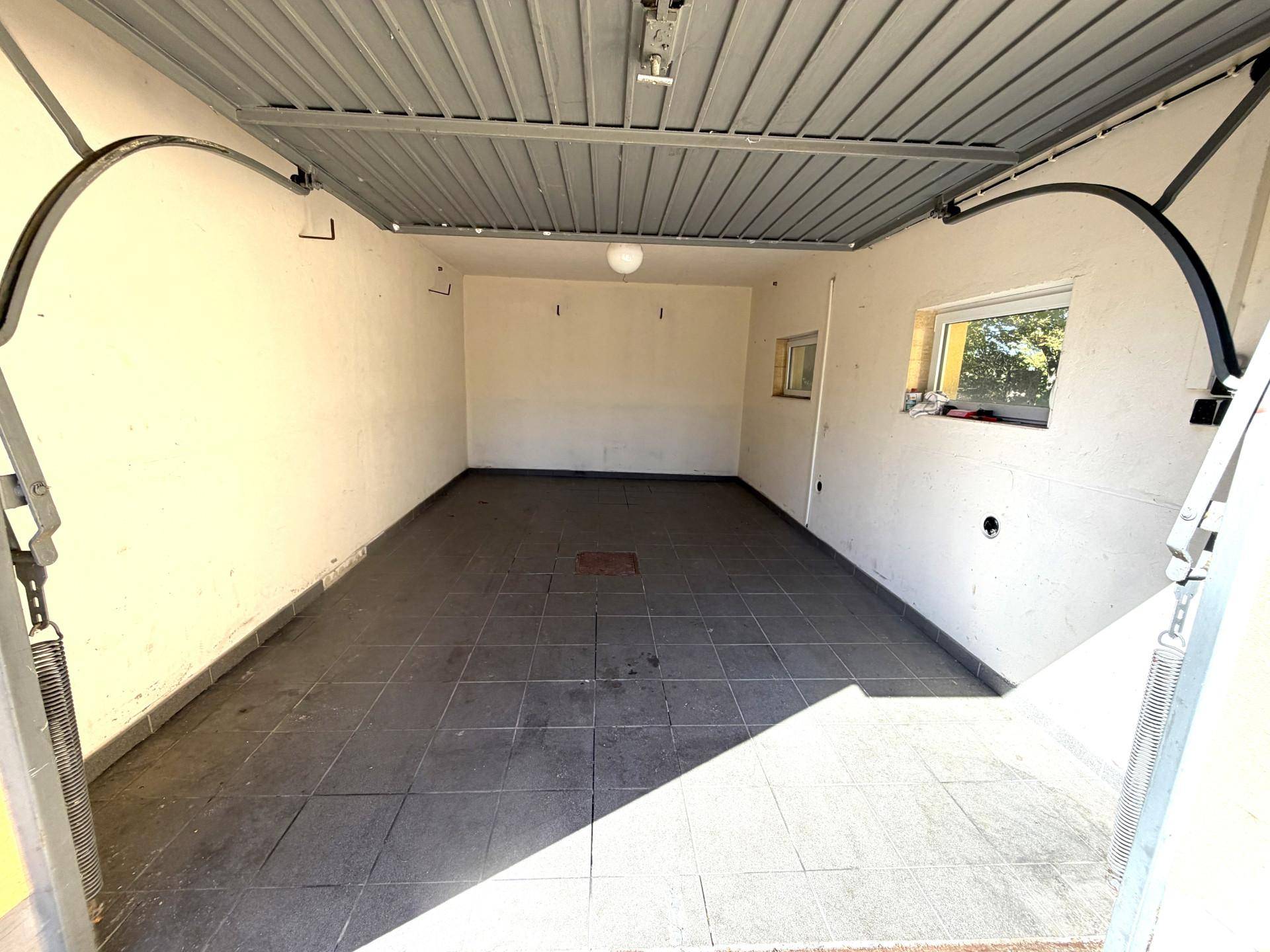 Leere Garage mit Fliesenboden und einem kleinen Fenster, bereit zur Nutzung.