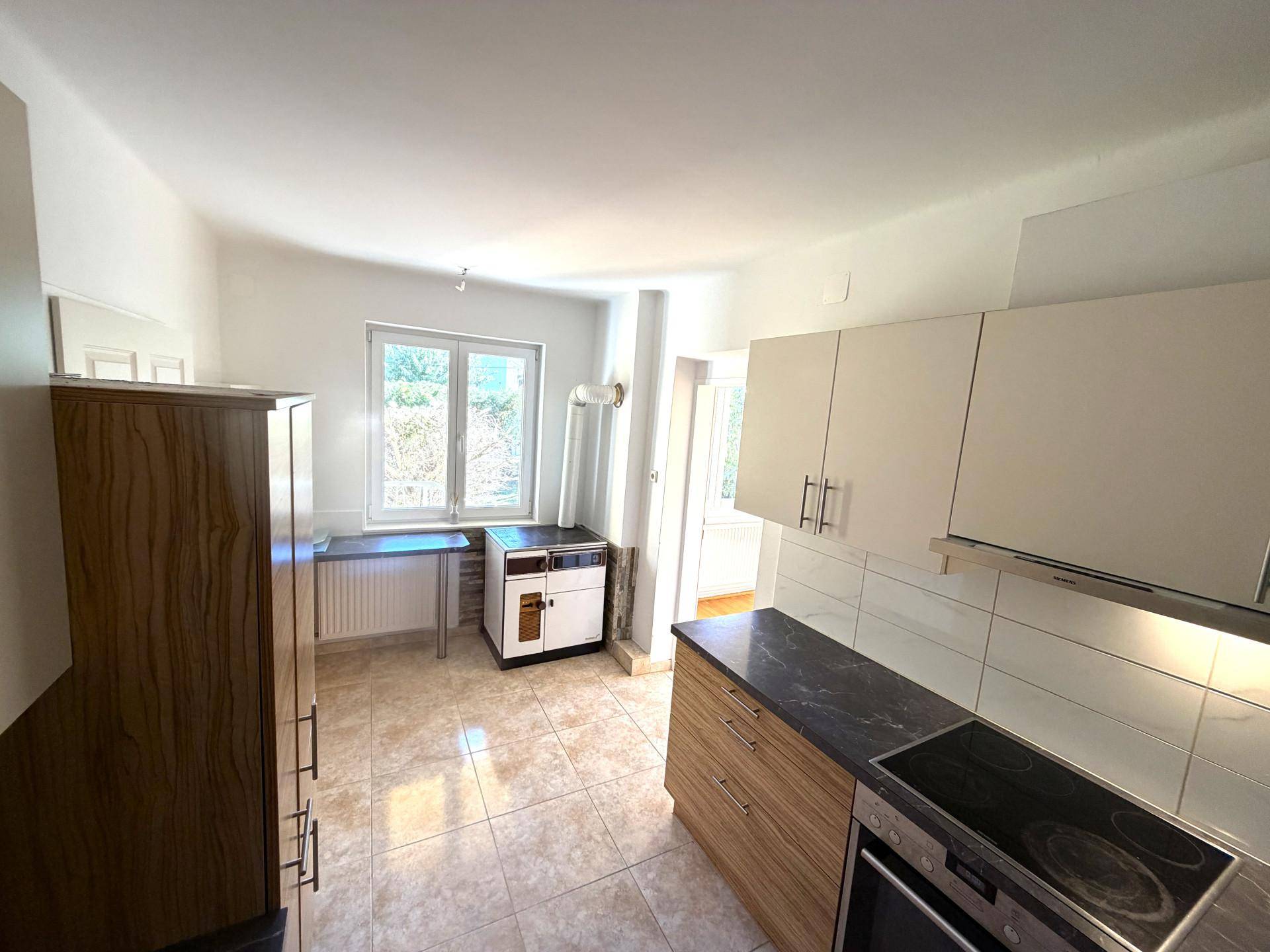 Funktionale Küche mit Fenster, hellen Schränken, dunkler Arbeitsplatte und Fliesenboden.