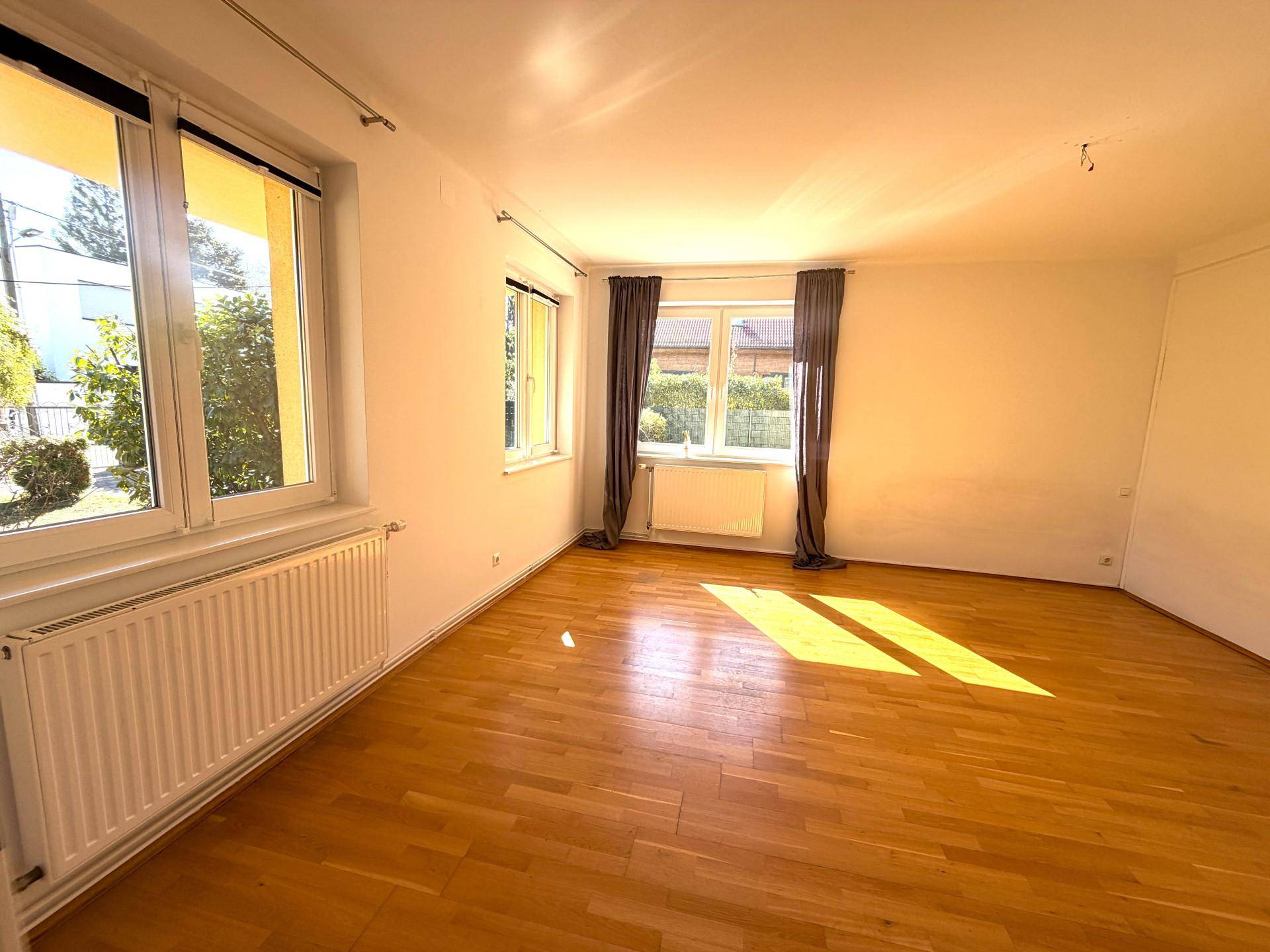 Lichtdurchflutetes Wohnzimmer mit Holzboden und großen Fenstern, die eine helle Atmosphäre schaffen.