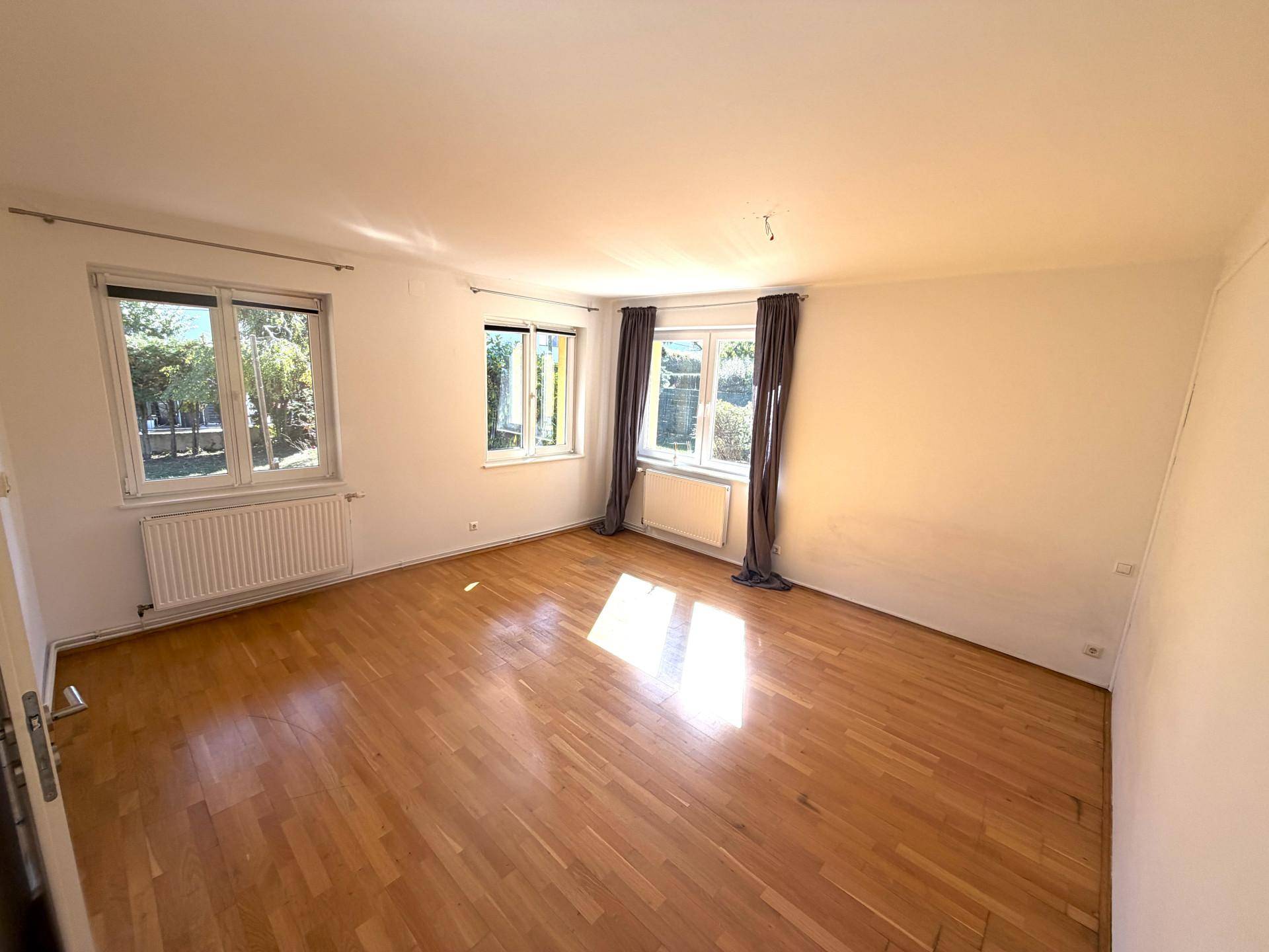 Helles Wohnzimmer mit Parkettboden und mehreren Fenstern, die viel Tageslicht hereinlassen.