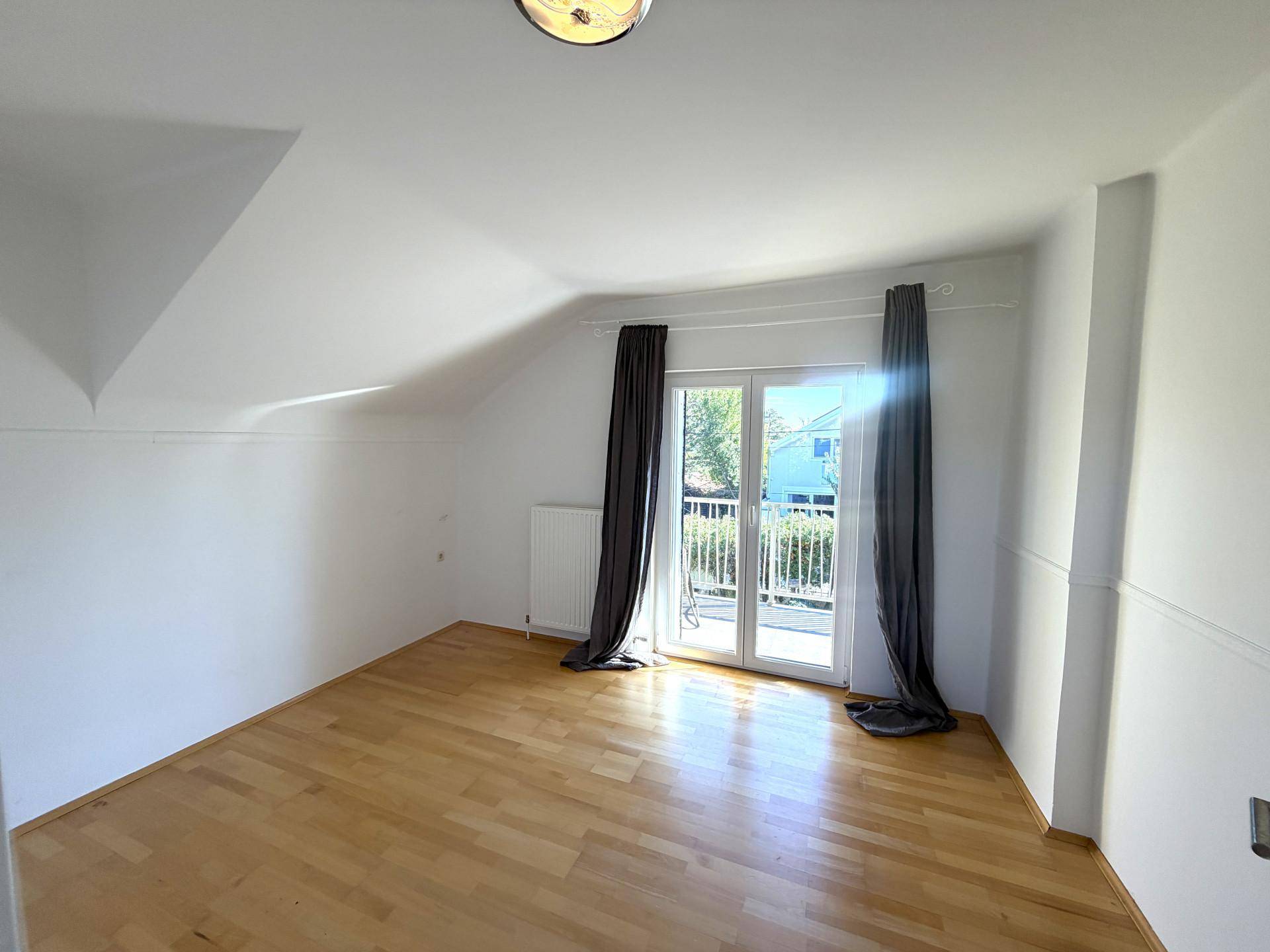 Schlafzimmer im Dachgeschoss mit hellem Holzboden, weißen Wänden und Zugang zu einem Balkon.