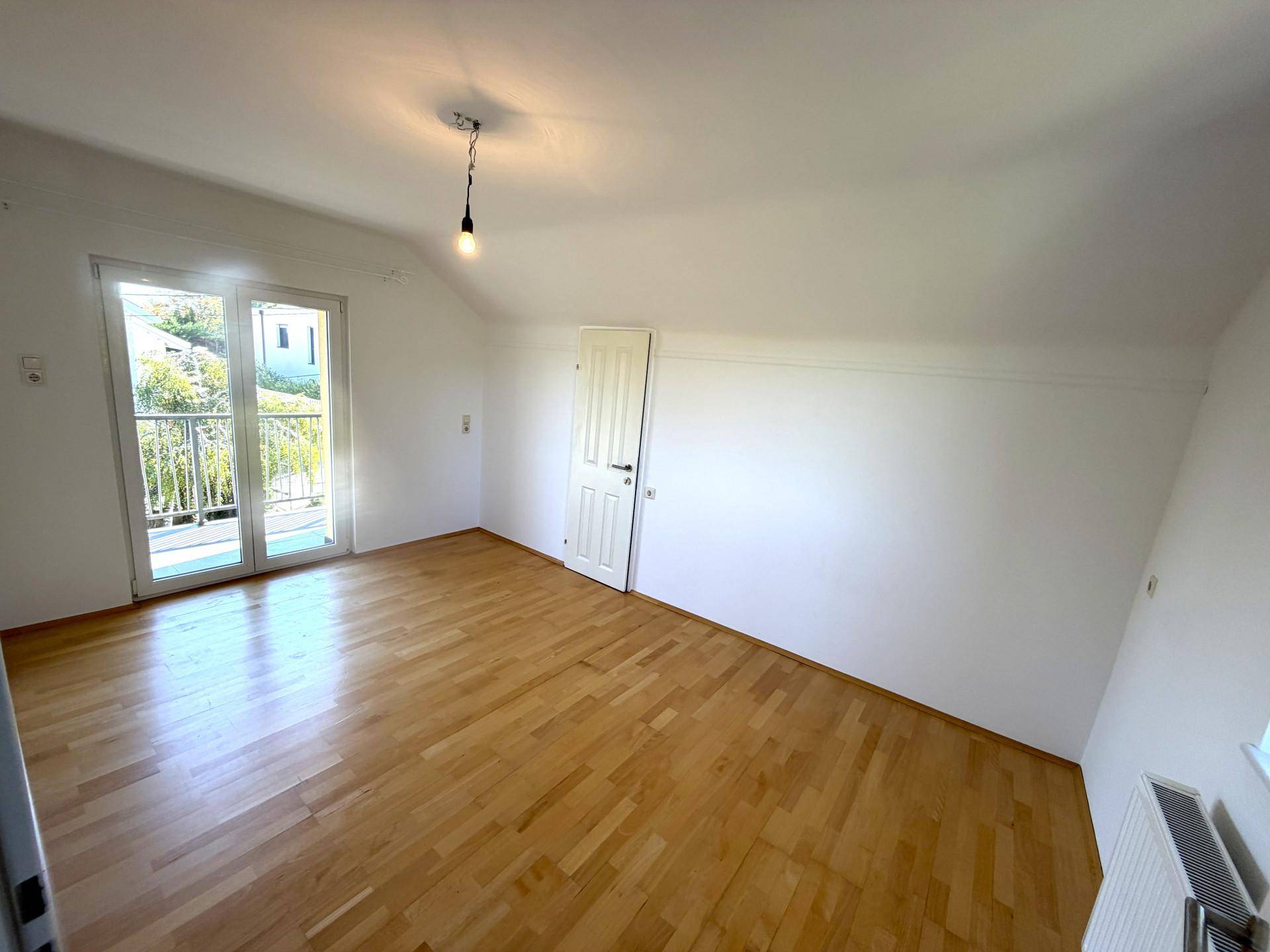 Geräumiges Schlafzimmer im Dachgeschoss mit Holzboden und direktem Zugang zum sonnigen Balkon.