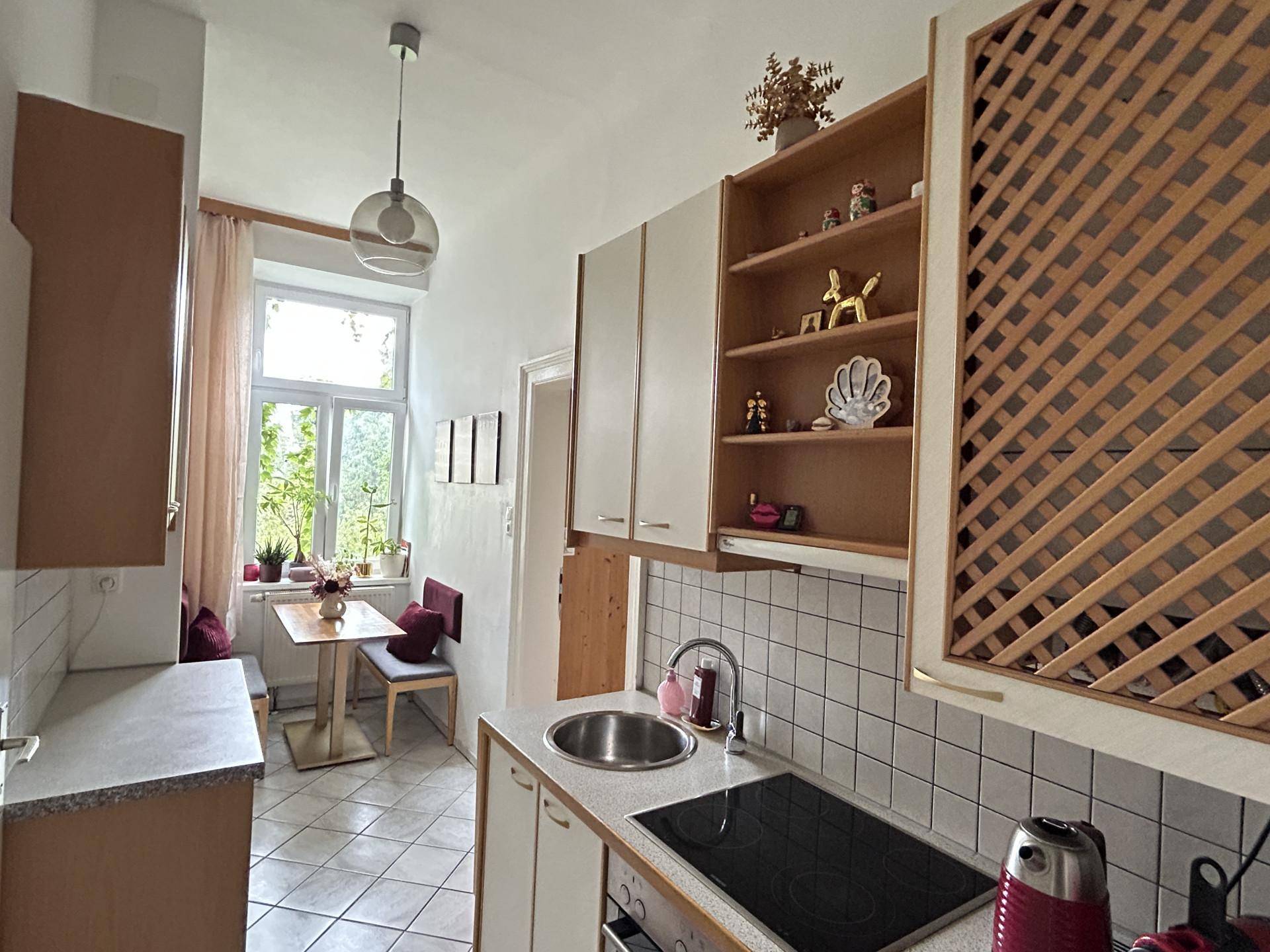 Helle Küche mit Essbereich am Fenster, weißen Fliesen und Holzschränken.