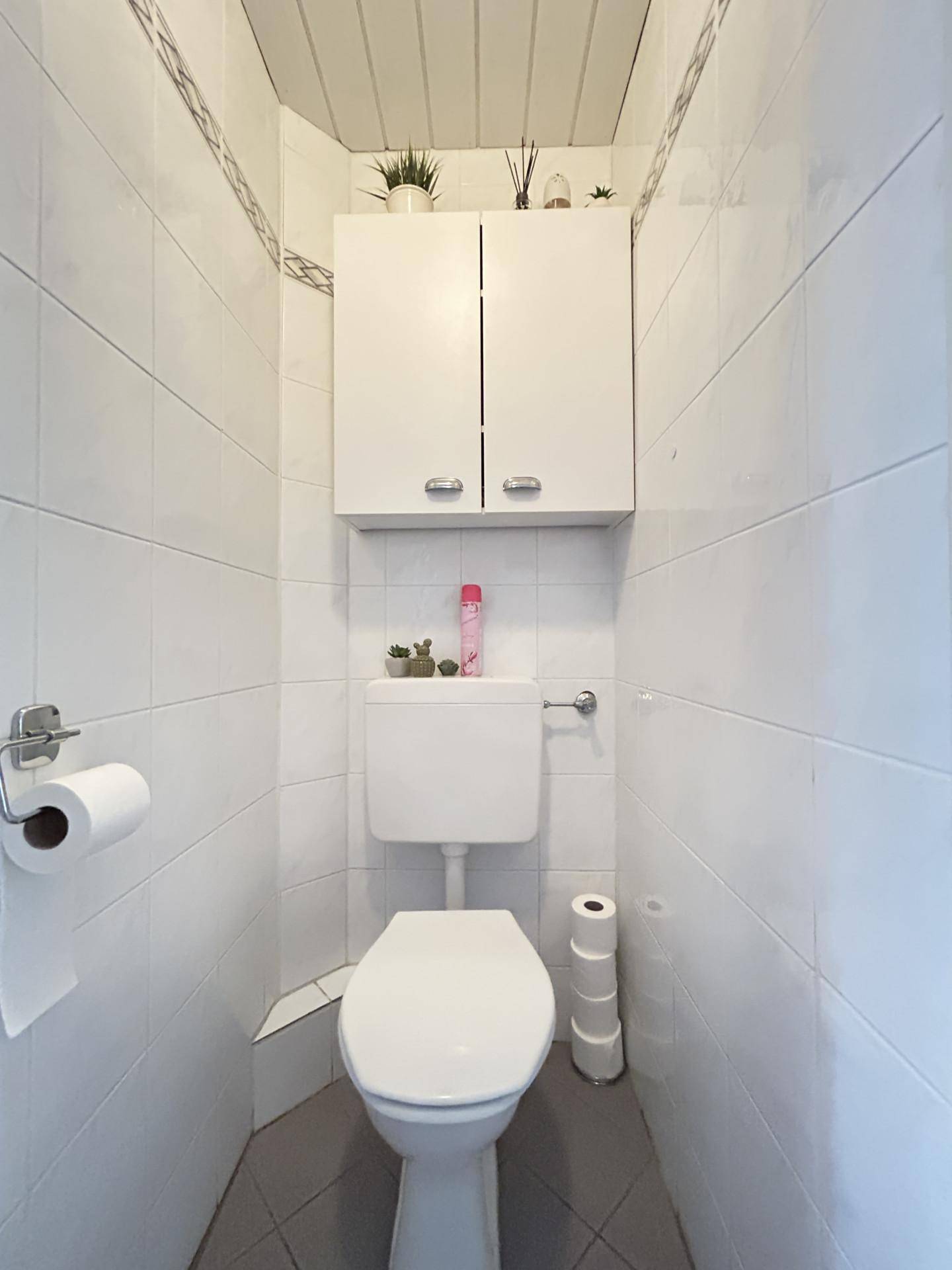 Separates WC mit Toilette und weißen Wandfliesen.