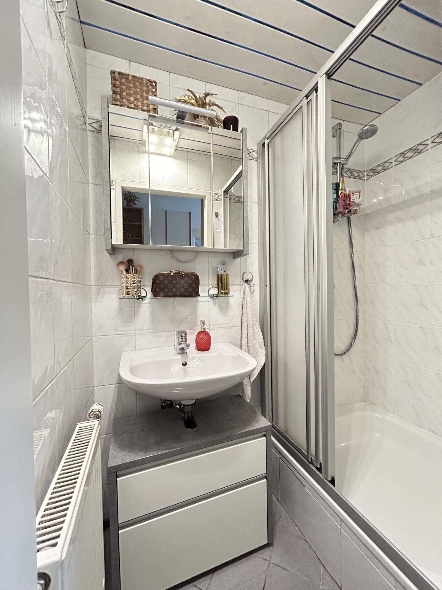 Kleines Badezimmer mit Dusche, Waschbecken und weißen Wandfliesen.