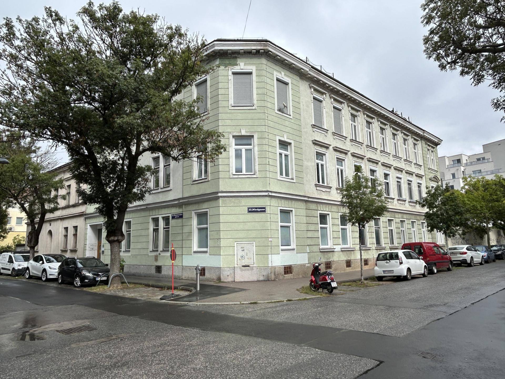 Eckgebäude mit klassischer Architektur, vielen Fenstern und Bäumen an der Straße.