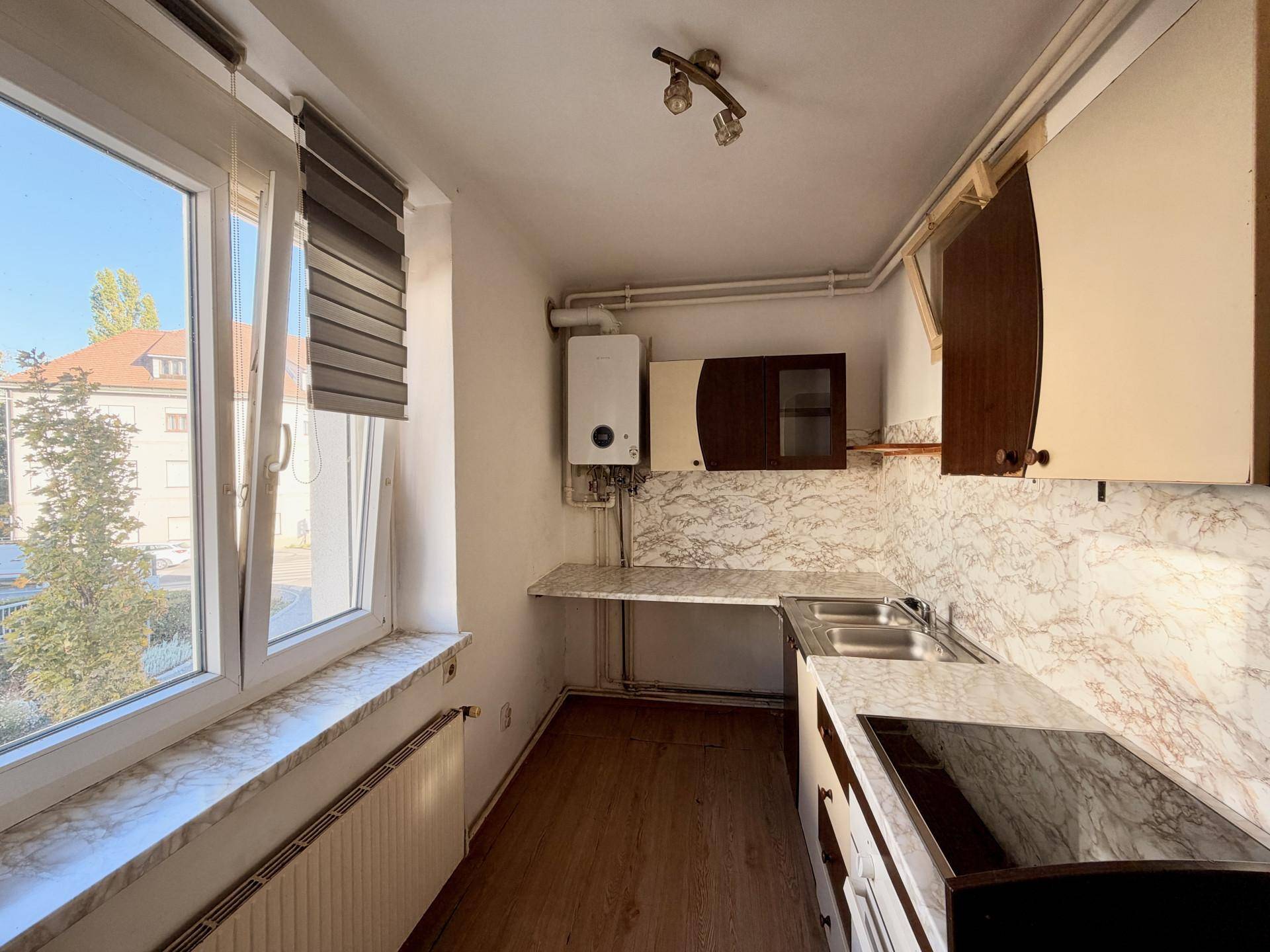 Kleine Küche mit Marmoroptik-Arbeitsplatten, Spüle, Kochfeld und einem Fenster mit Blick ins Grüne.