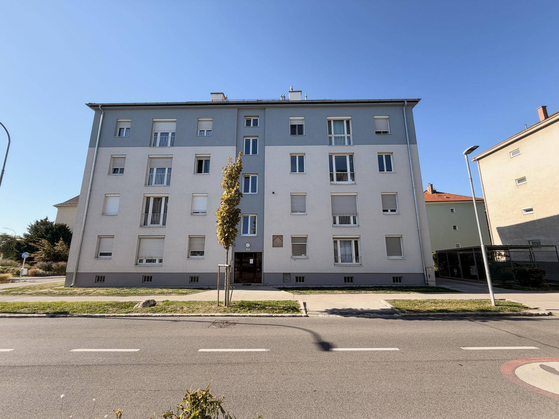 Mehrfamilienhaus mit moderner Fassade in Grau- und Weißtönen an einer Straße gelegen.