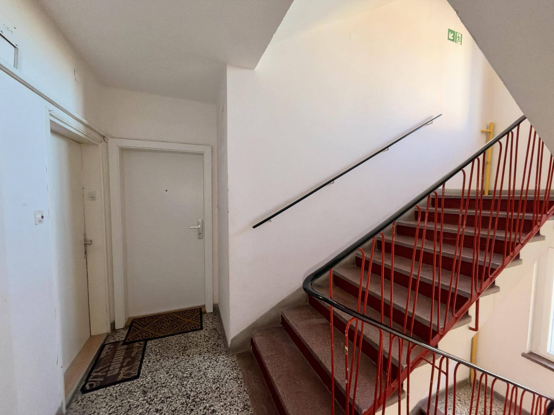 Treppenhaus mit rotem Geländer und Terrazzoboden in einem Mehrfamilienhaus.