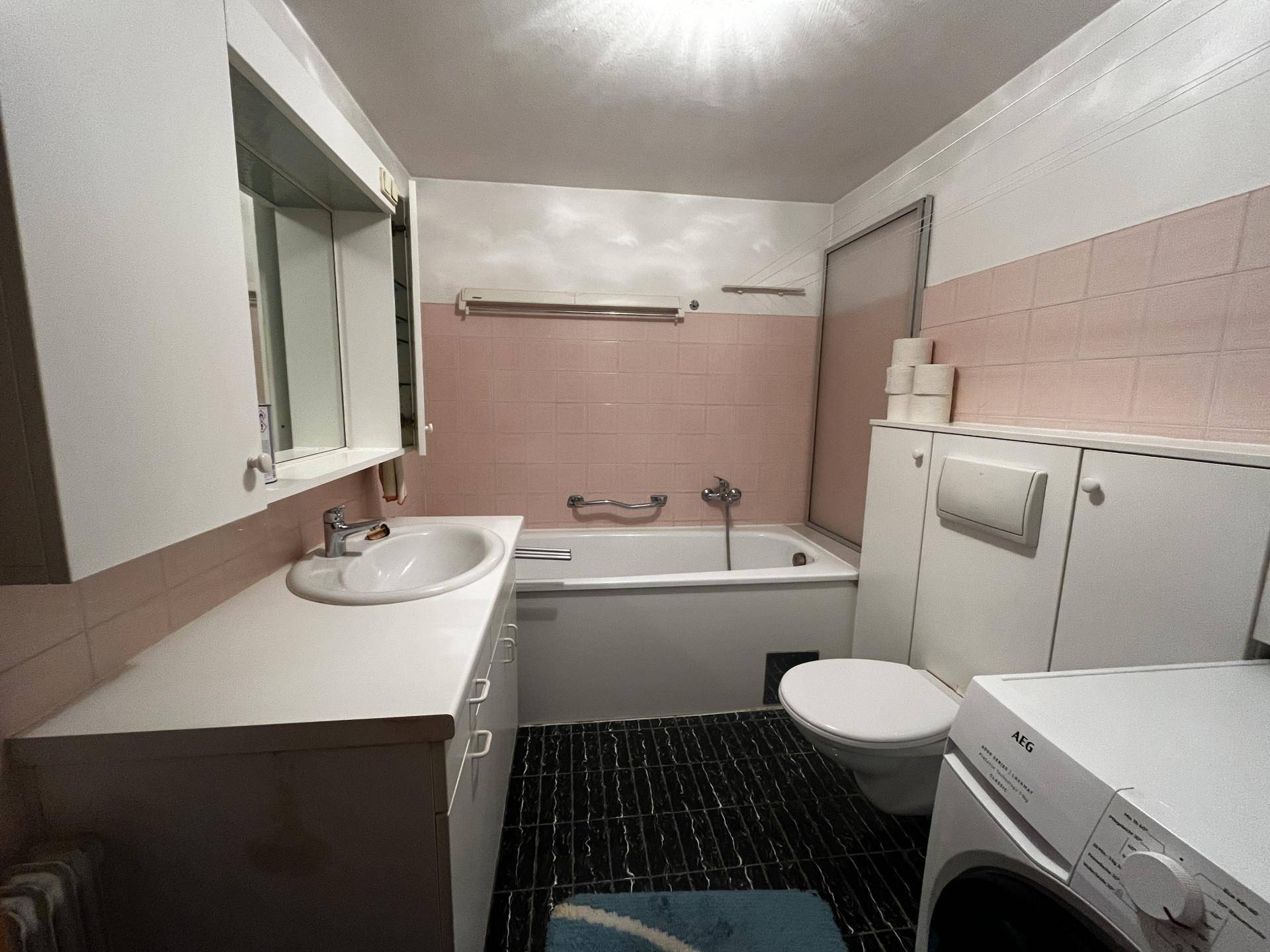 Badezimmer im 80er-Jahre-Stil mit rosa Fliesen, Badewanne und integrierter Waschmaschine.