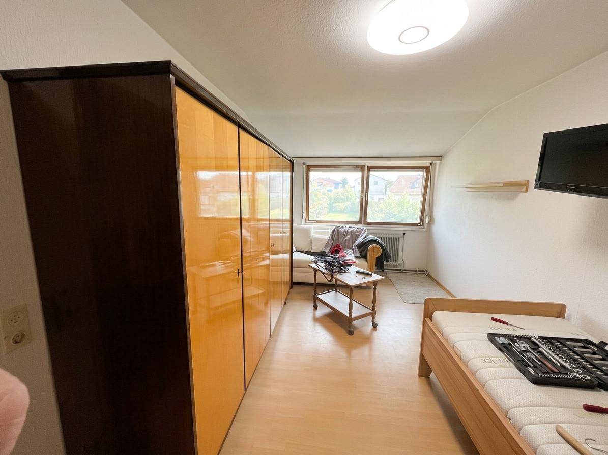 Schlafzimmer mit hellem Laminatboden, großem Kleiderschrank und einem Fenster mit Blick ins Grüne.