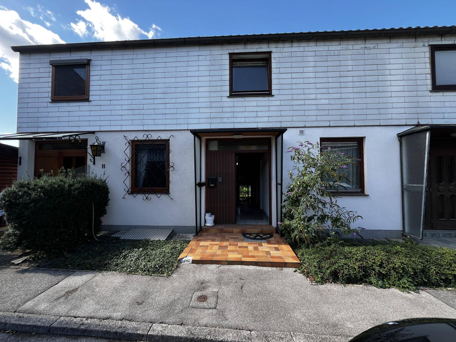 Vorderansicht eines Reihenhauses mit weißer Fassade, braunen Fenstern und einem kleinen Vorgarten.