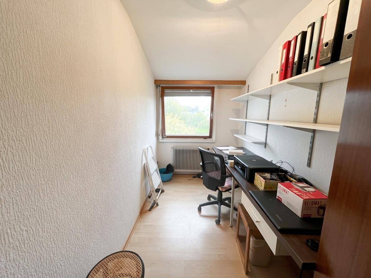 Kleines Arbeitszimmer mit hellem Laminatboden, Regalwänden und einem Fenster für Tageslicht.