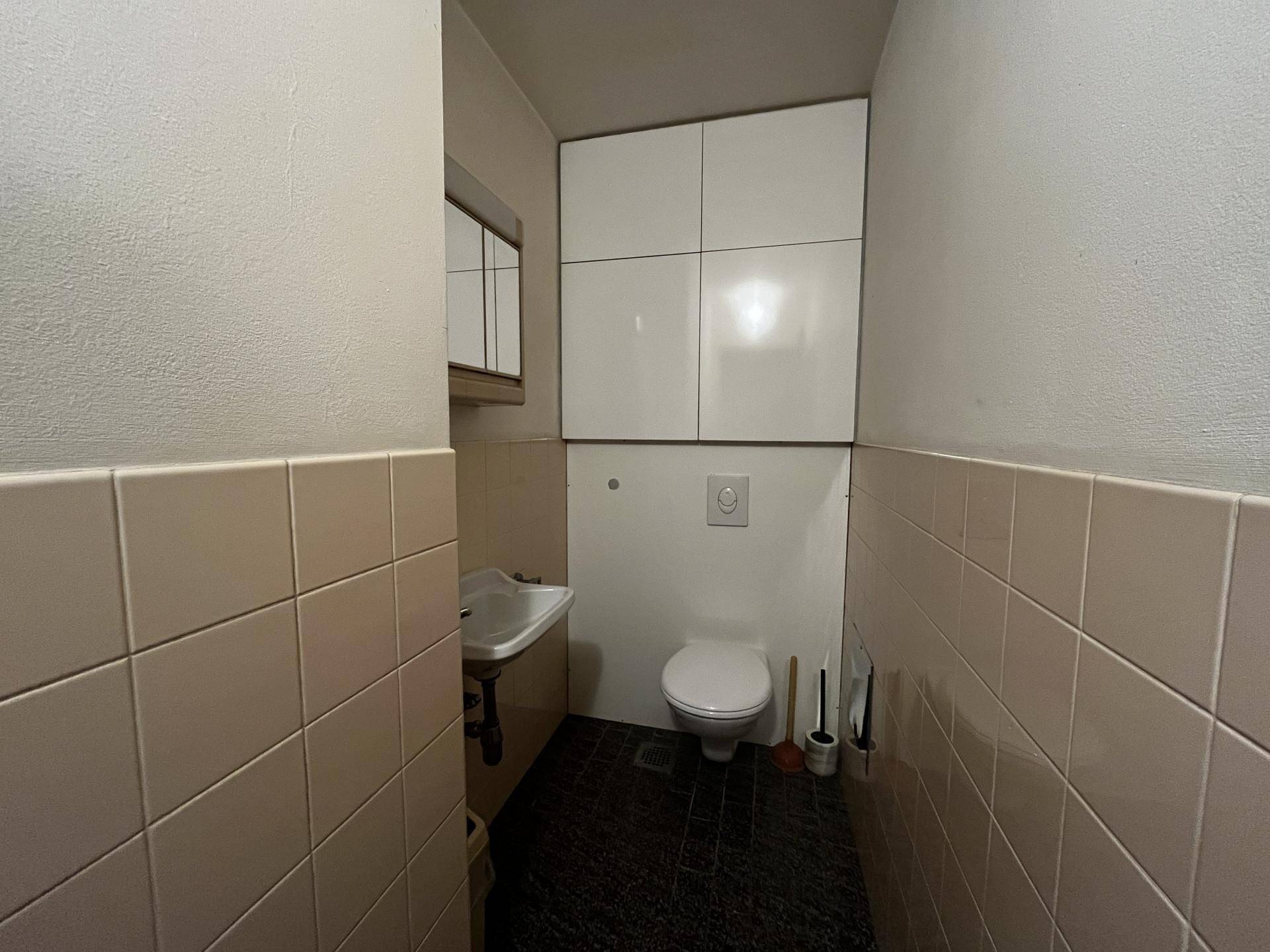 Kleines Gäste-WC mit Wand-WC, Waschbecken und weißen Hängeschränken.