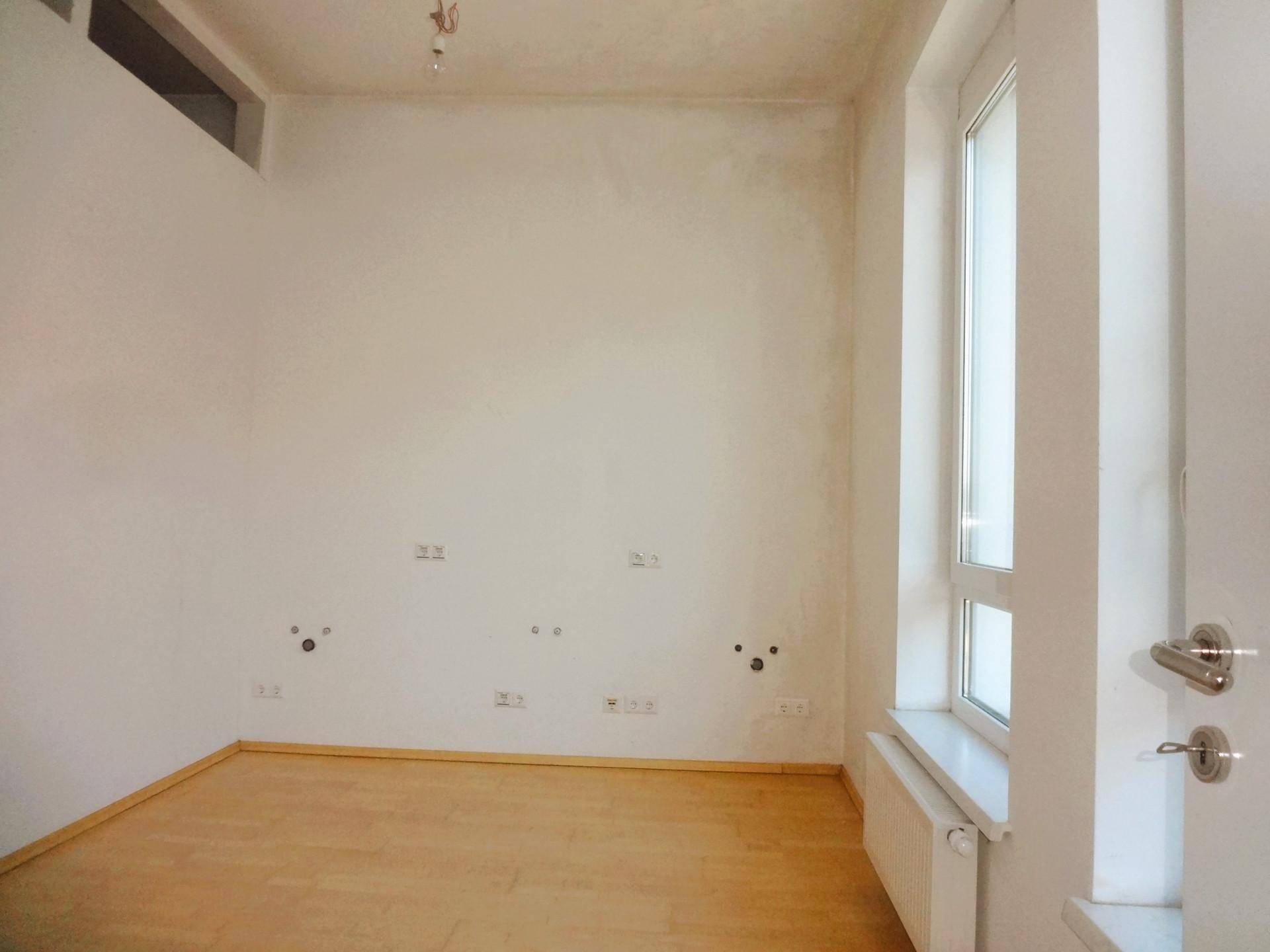 Heller, unmöblierter Raum mit Parkettboden, einem Fenster und zahlreichen Steckdosen an der Wand.