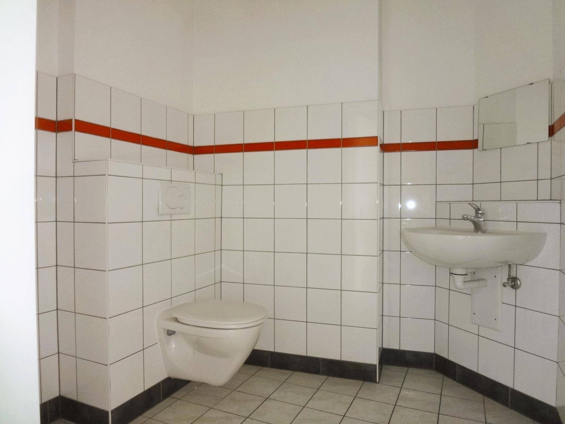 Gefliestes Badezimmer mit Toilette, Waschbecken und einer markanten orangefarbenen Zierleiste.