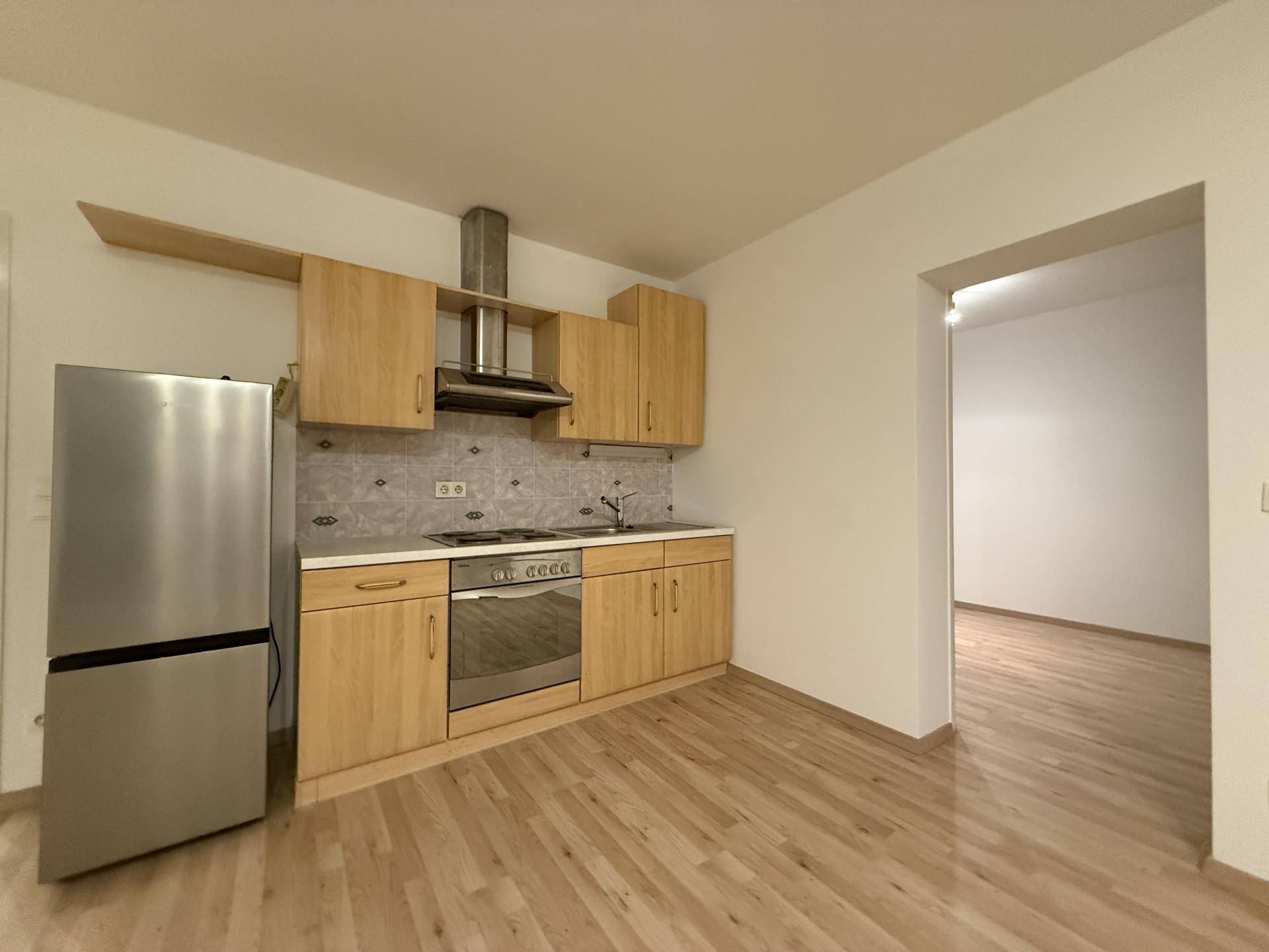 Kleine Einbauküche mit Holzfronten, Edelstahlgeräten und hellem Laminatboden.