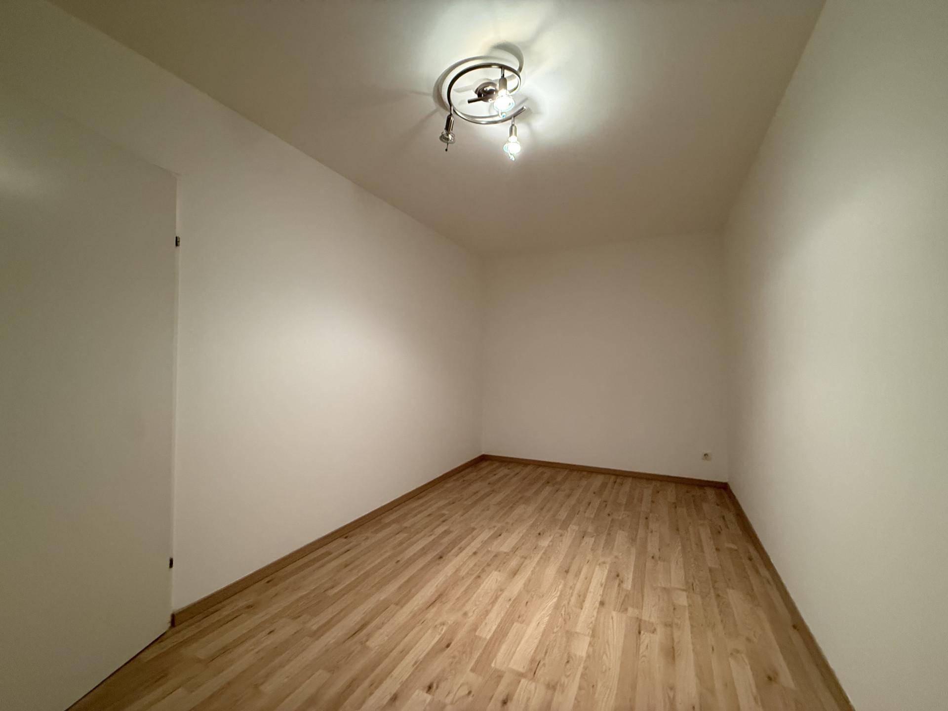 Leerer Raum mit hellem Laminatboden und weißen Wänden, bereit zur individuellen Gestaltung.