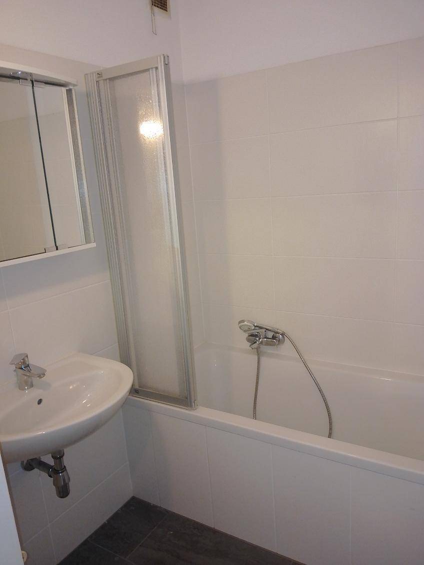 Helles Badezimmer mit Badewanne, Duschwand, Waschbecken und Spiegelschrank, weiß gefliest.