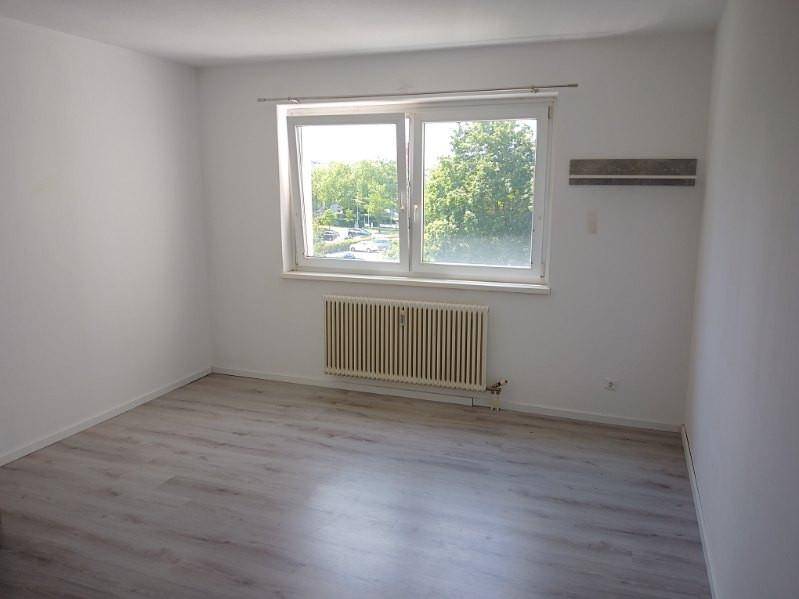Heller, leerer Raum mit großem Fenster und Blick ins Grüne, ausgestattet mit Heizkörper.