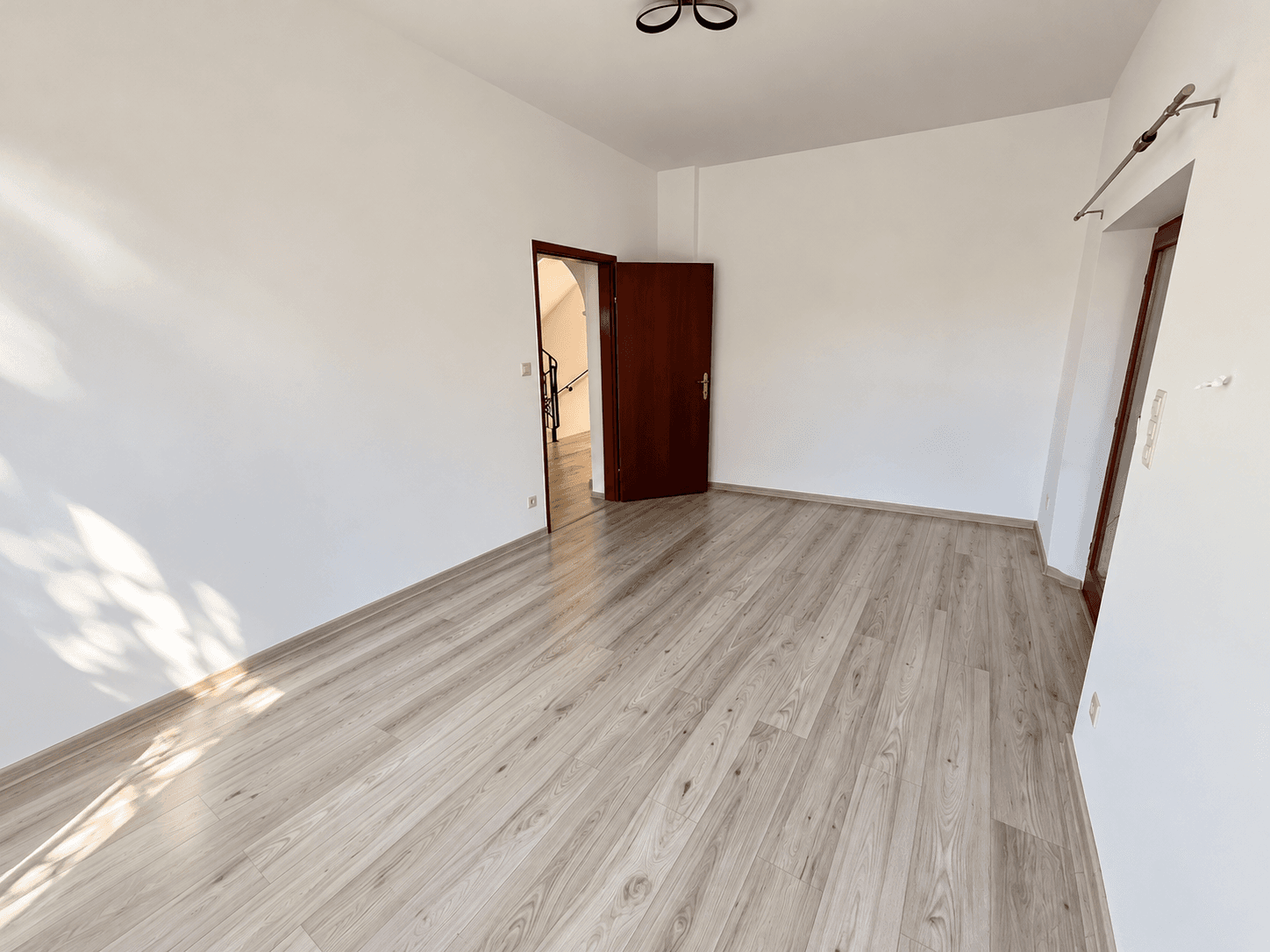 Leerer Raum mit hellem Laminatboden und Zugang zu weiteren Bereichen des Hauses.