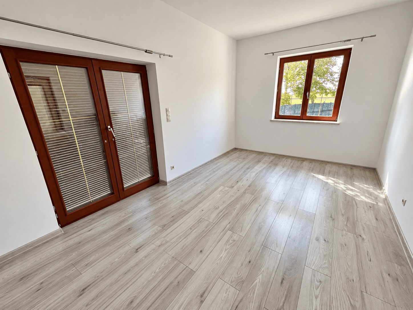 Heller Raum mit modernem Laminatboden und einem Fenster, bereit zur individuellen Gestaltung.